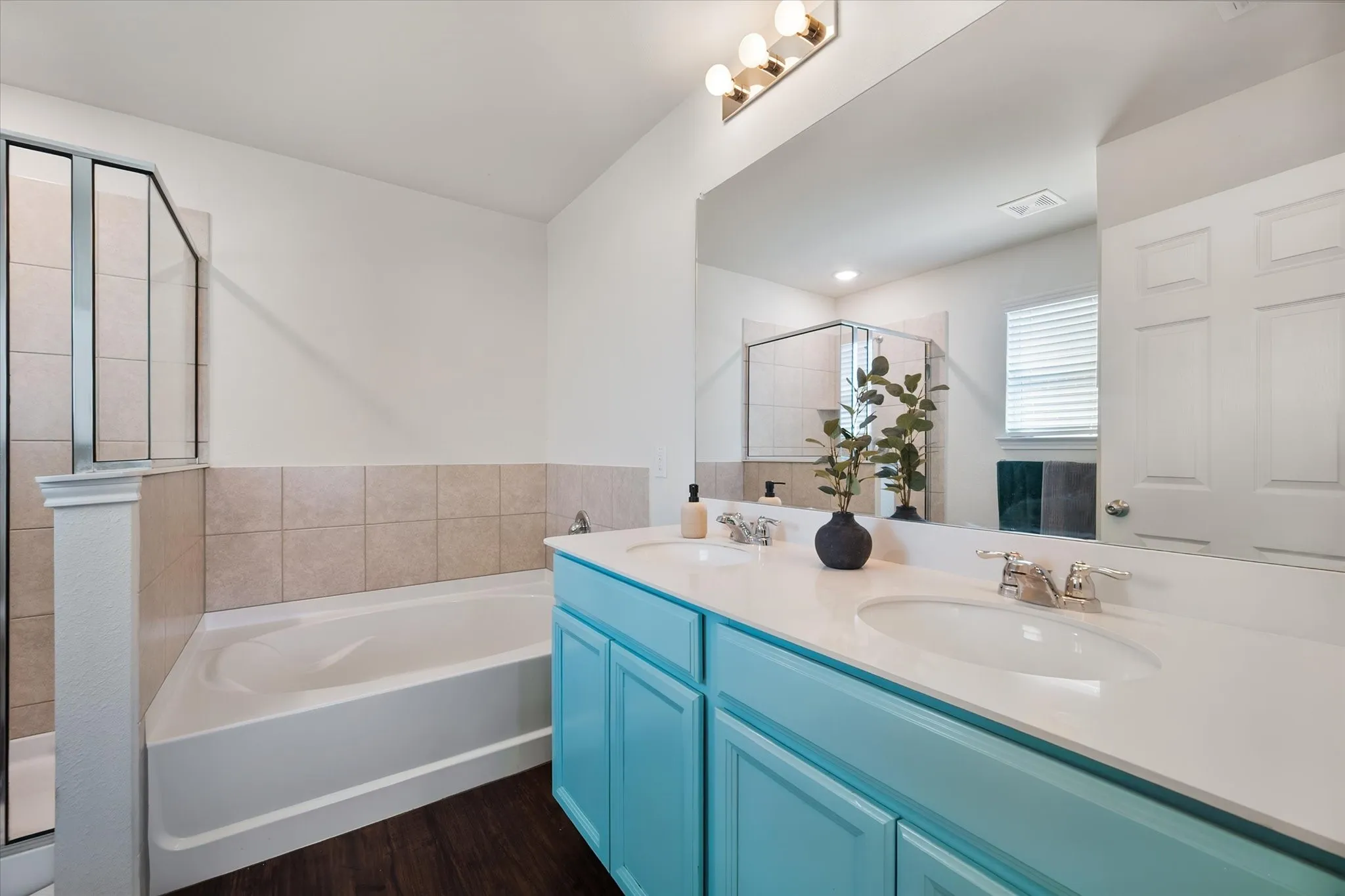 Dual vanity with integrated sinks, spacious mirror, contemporary light fixture, built-in tub, and separate glass-enclosed shower