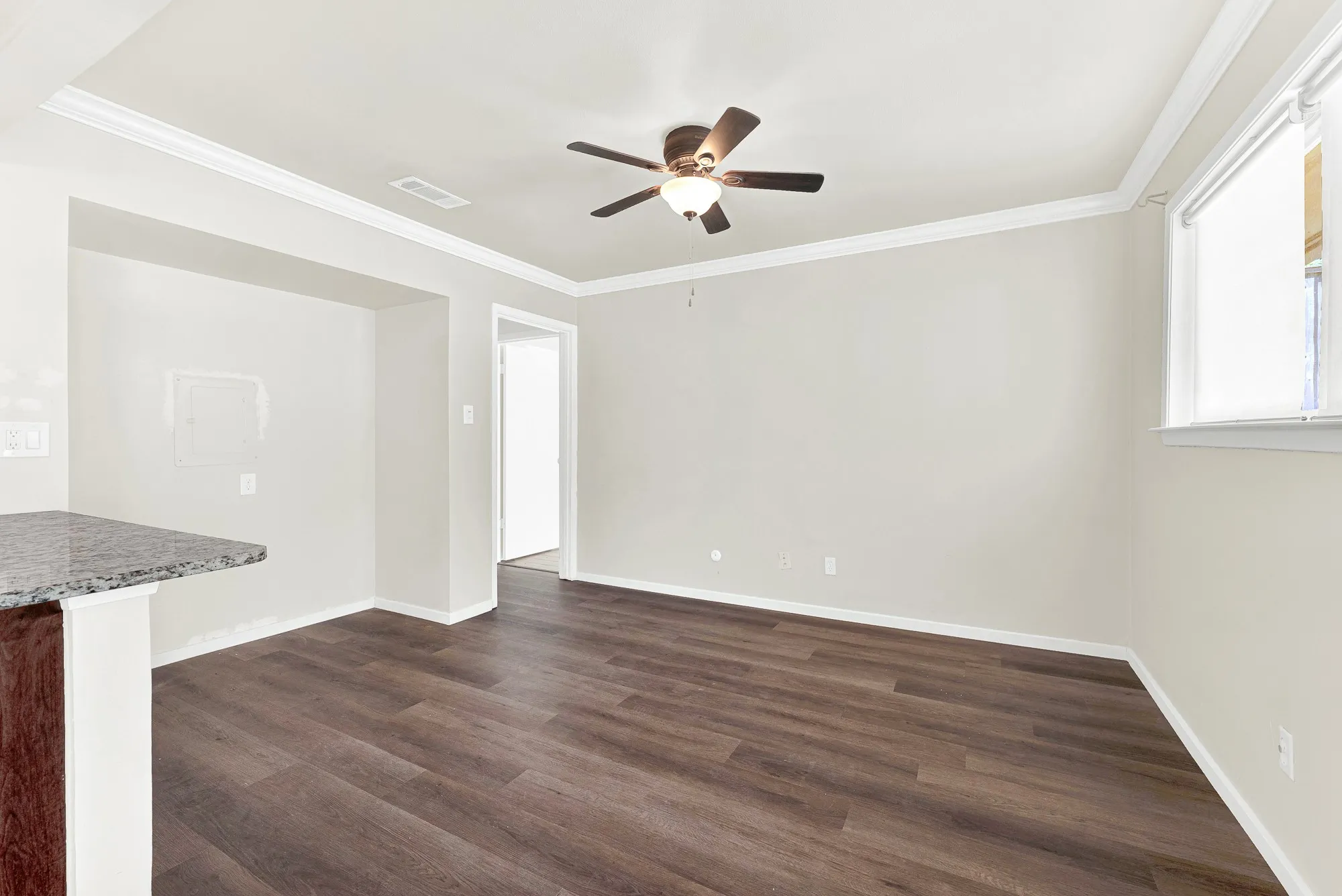 Spacious interior with wood-finish flooring, a ceiling fan, crown molding, and a partial granite-top breakfast bar