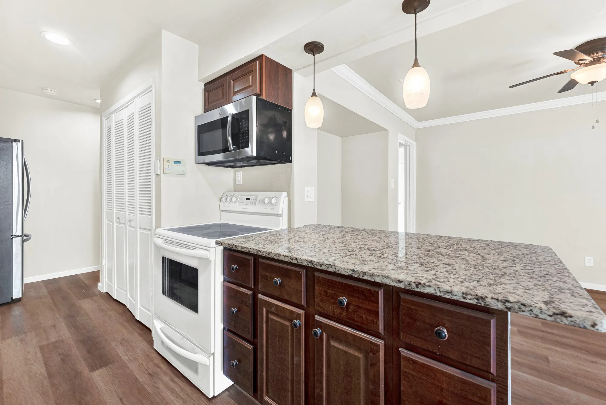Kitchen featuring wood-finish flooring, dark wood cabinetry, a stone countertop island, stainless steel microwave, and white electric range