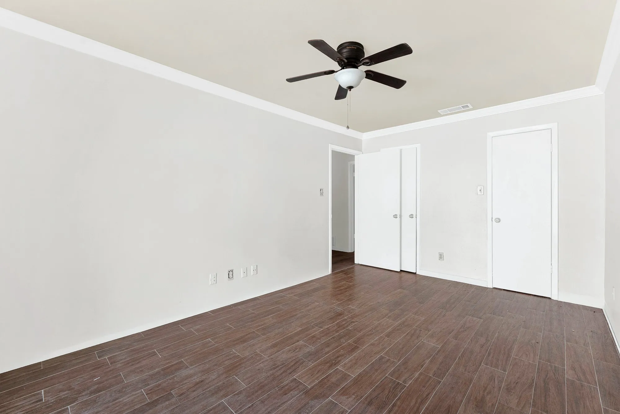 Wood-finish flooring, ceiling fan, crown molding, and white walls
