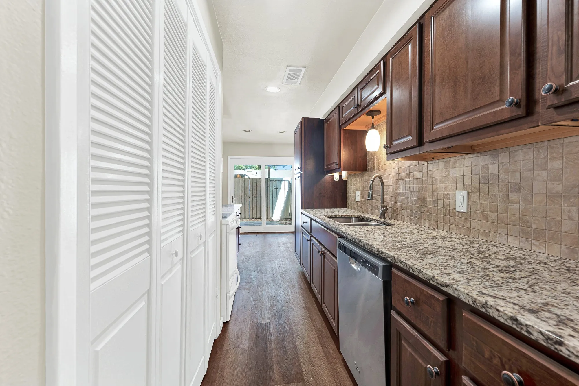 Kitchen featuring granite countertops, wood-finish flooring, stainless steel dishwasher, wood cabinetry, and a tile backsplash