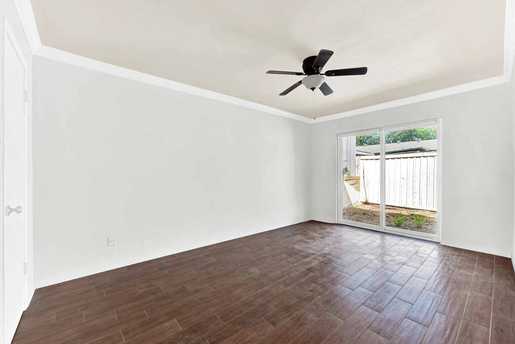 Spacious room with wood-finish tile flooring, ceiling fan with light fixture, and white trim