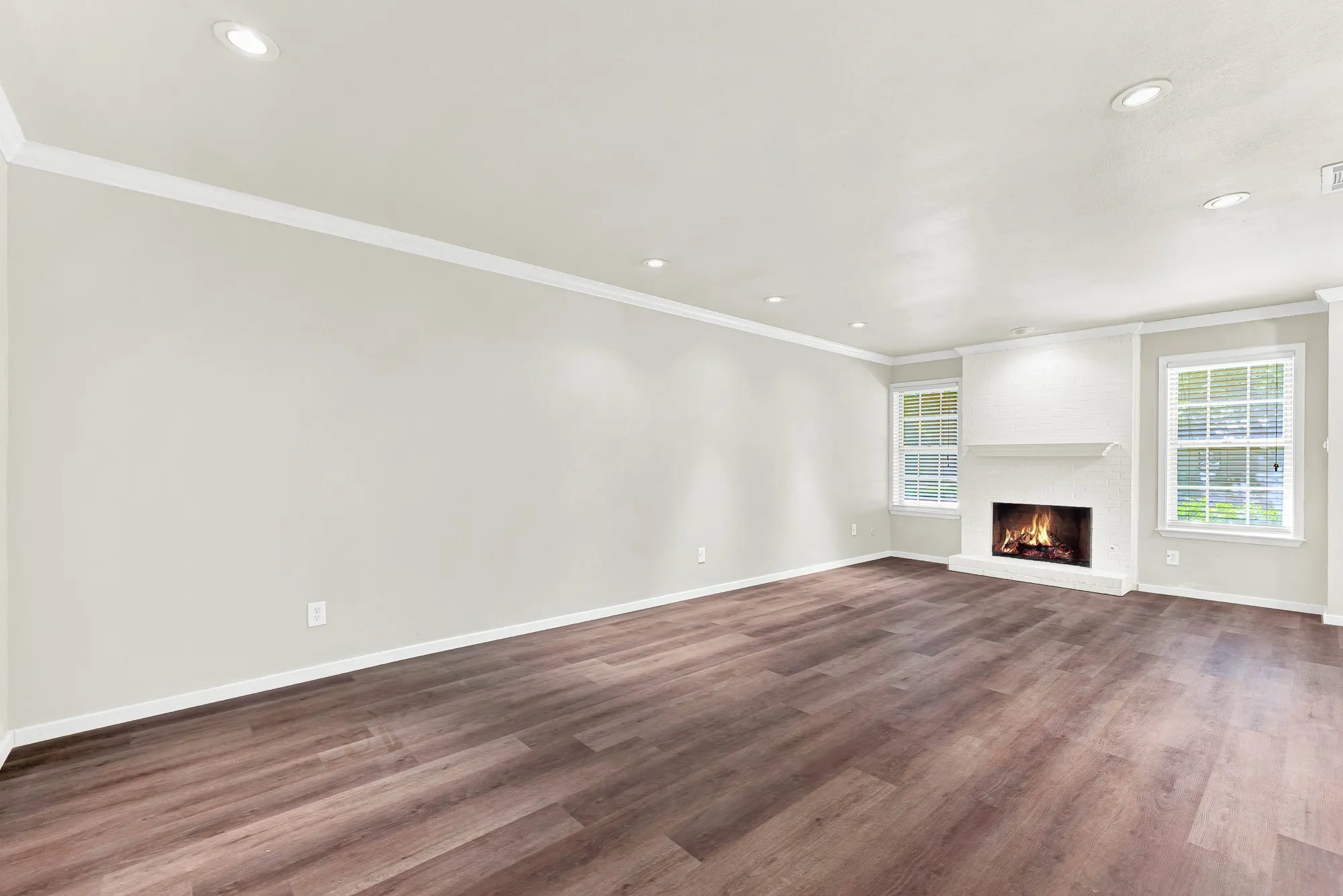 Spacious room featuring wood-finish flooring, recessed lighting, crown molding, and a brick fireplace
