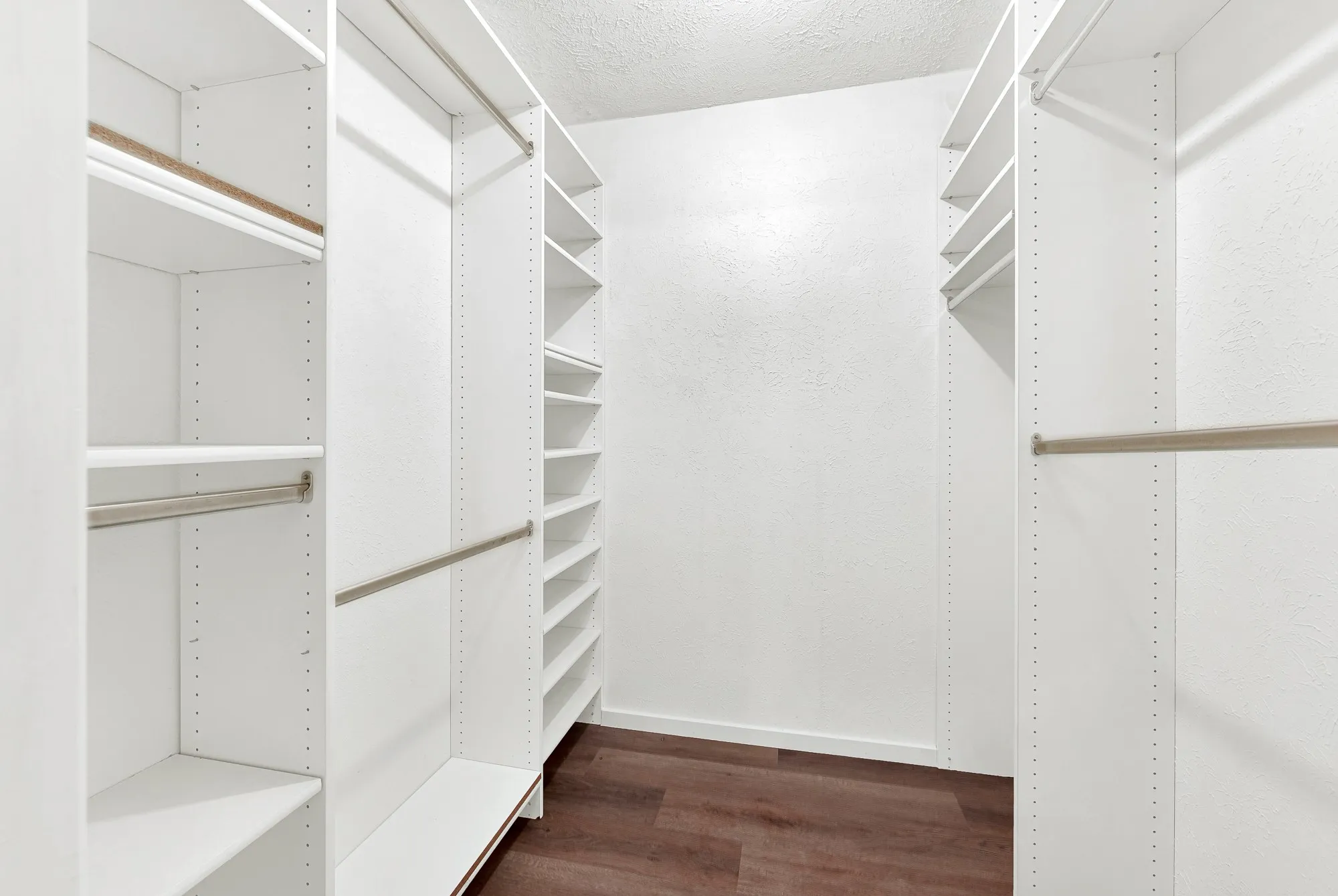 Walk-in closet featuring white built-in shelving, multiple hanging rods, and wood-finish flooring