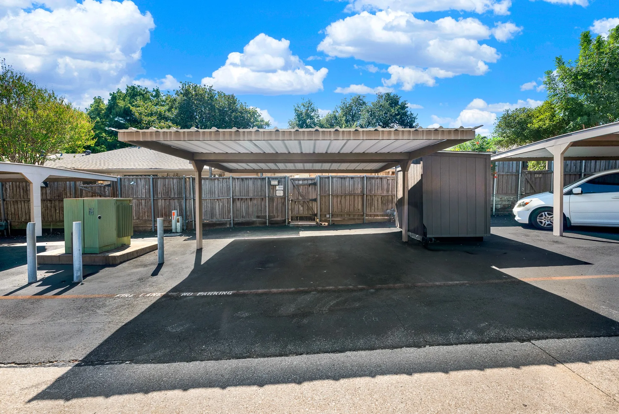 Modern utility courtyard featuring a spacious asphalt pad, overhead metal carport structure with integrated shade coverage, and multiple wooden storage enclosures