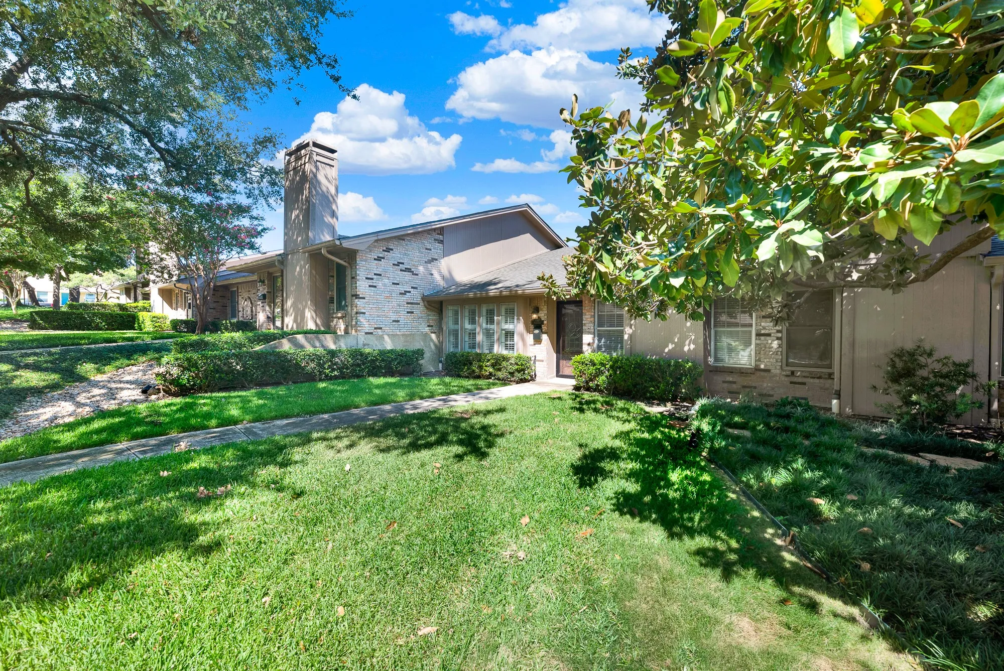 Traditional exterior with a stone and stucco facade, prominent chimney, mature trees, manicured lawn, and established shrubbery