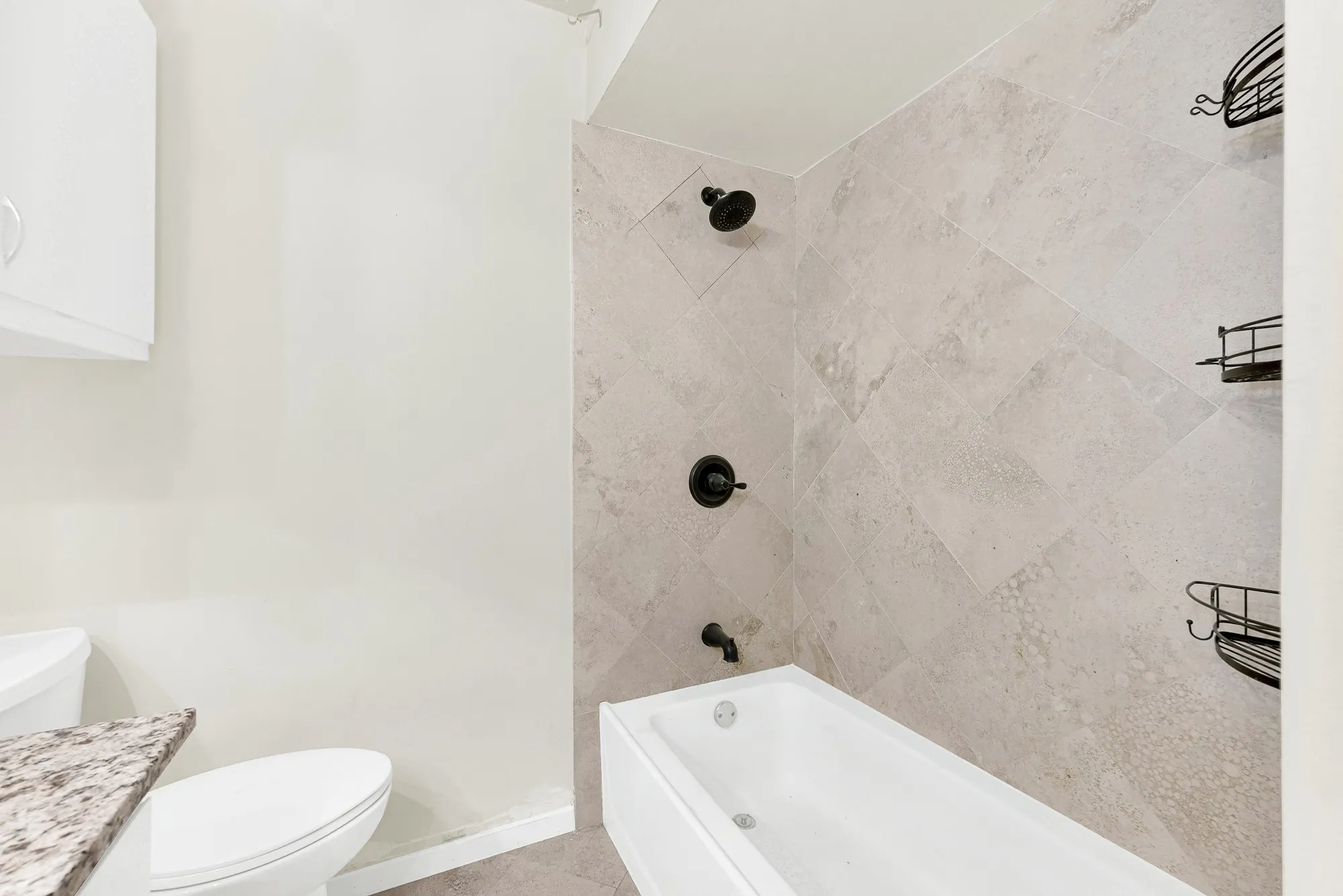 Bathtub with matte black fixtures, light-toned shower wall tile, and a built-in white cabinet