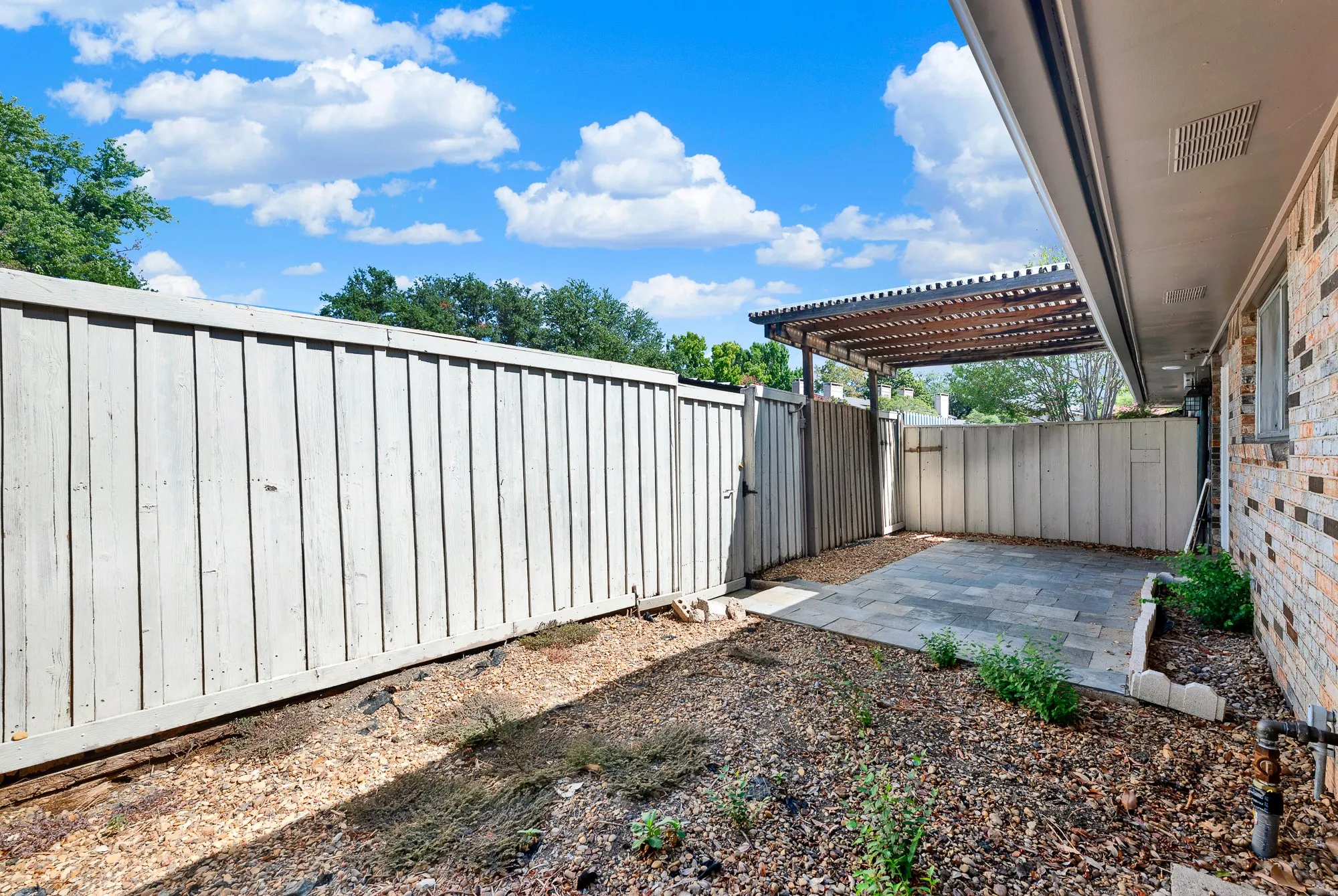 Private side yard featuring a wood fence, paver patio, slatted pergola, and brick exterior