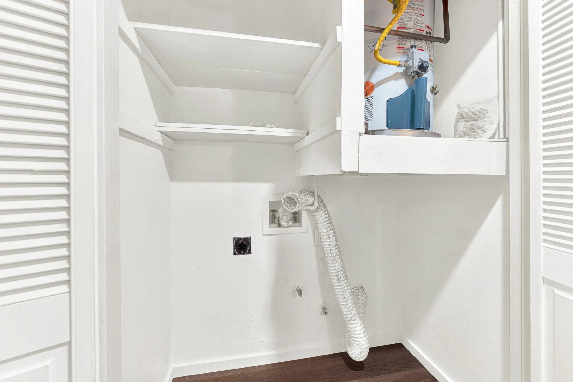 Louvered bi-fold doors, built-in shelving, water heater, and wood-finish flooring