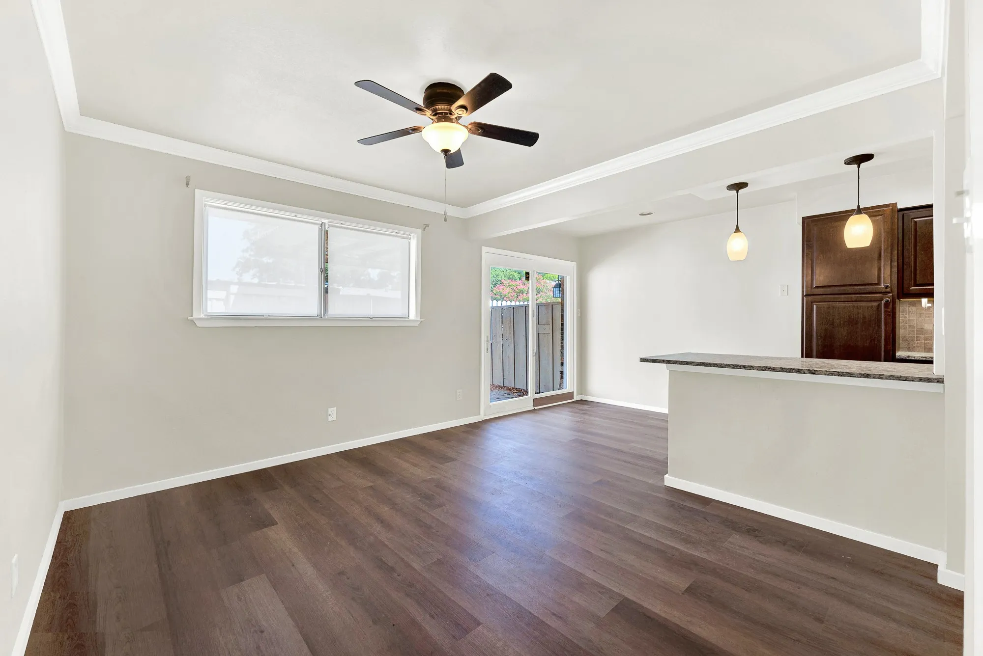Wood-finish flooring throughout, crown molding, ceiling fan with integrated lighting, sliding glass door, and a kitchen pass-through with pendant lighting