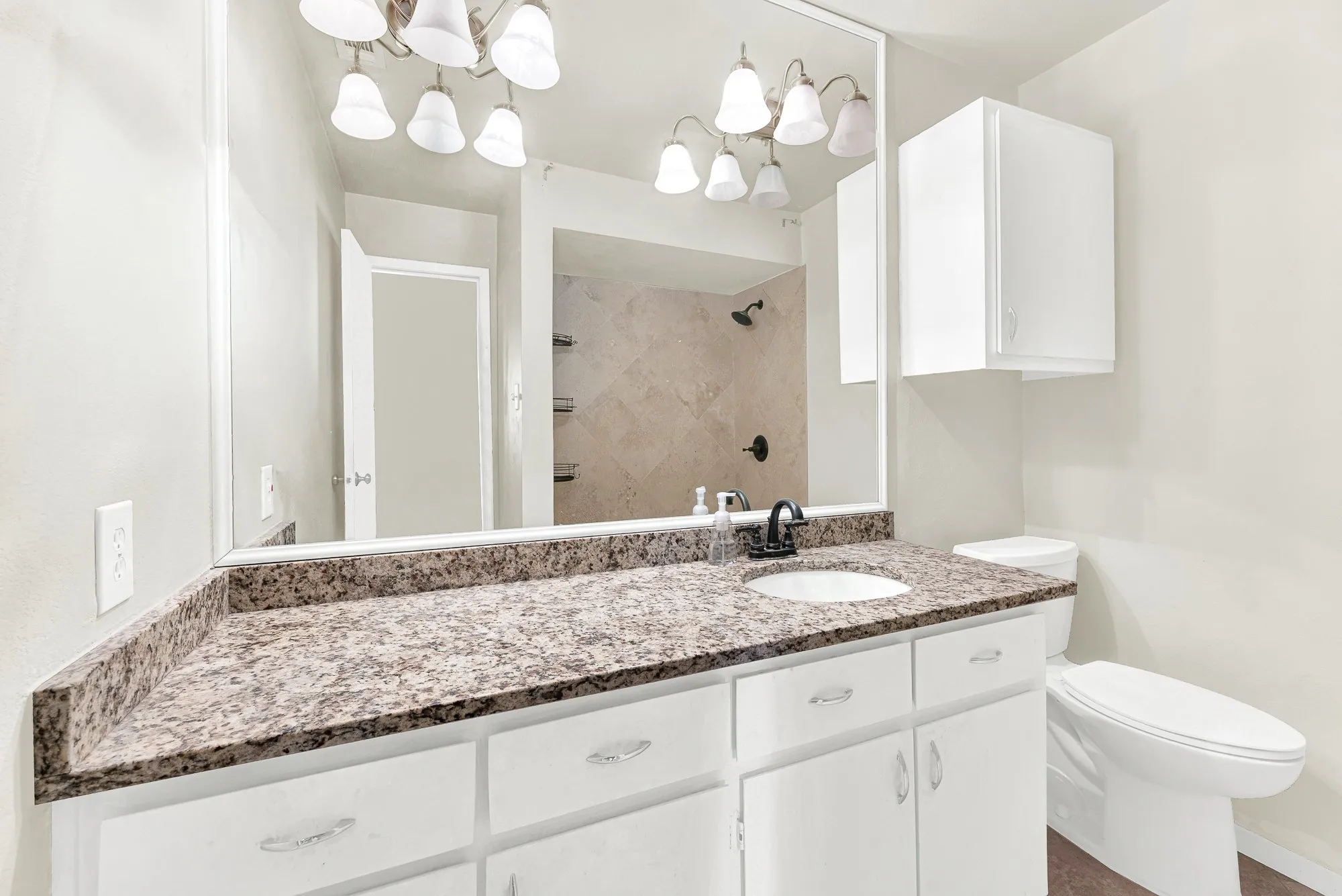 White vanity with a single basin sink, speckled stone countertop, large wall-mounted mirror, and overhead sconce lighting