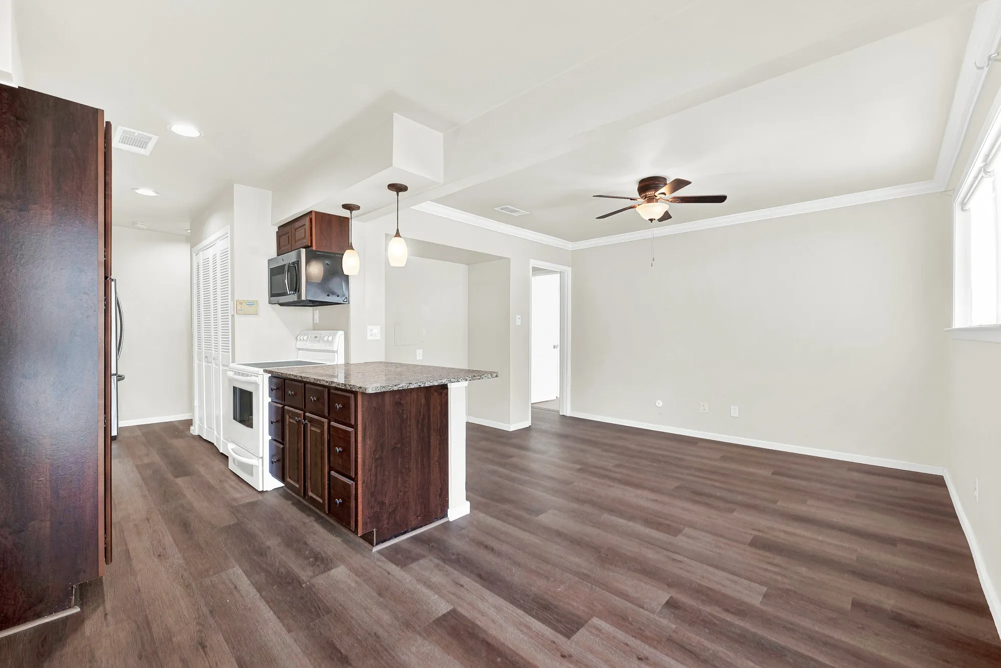 Open-concept living space with wood-finish flooring, a kitchen island, and a built-in microwave