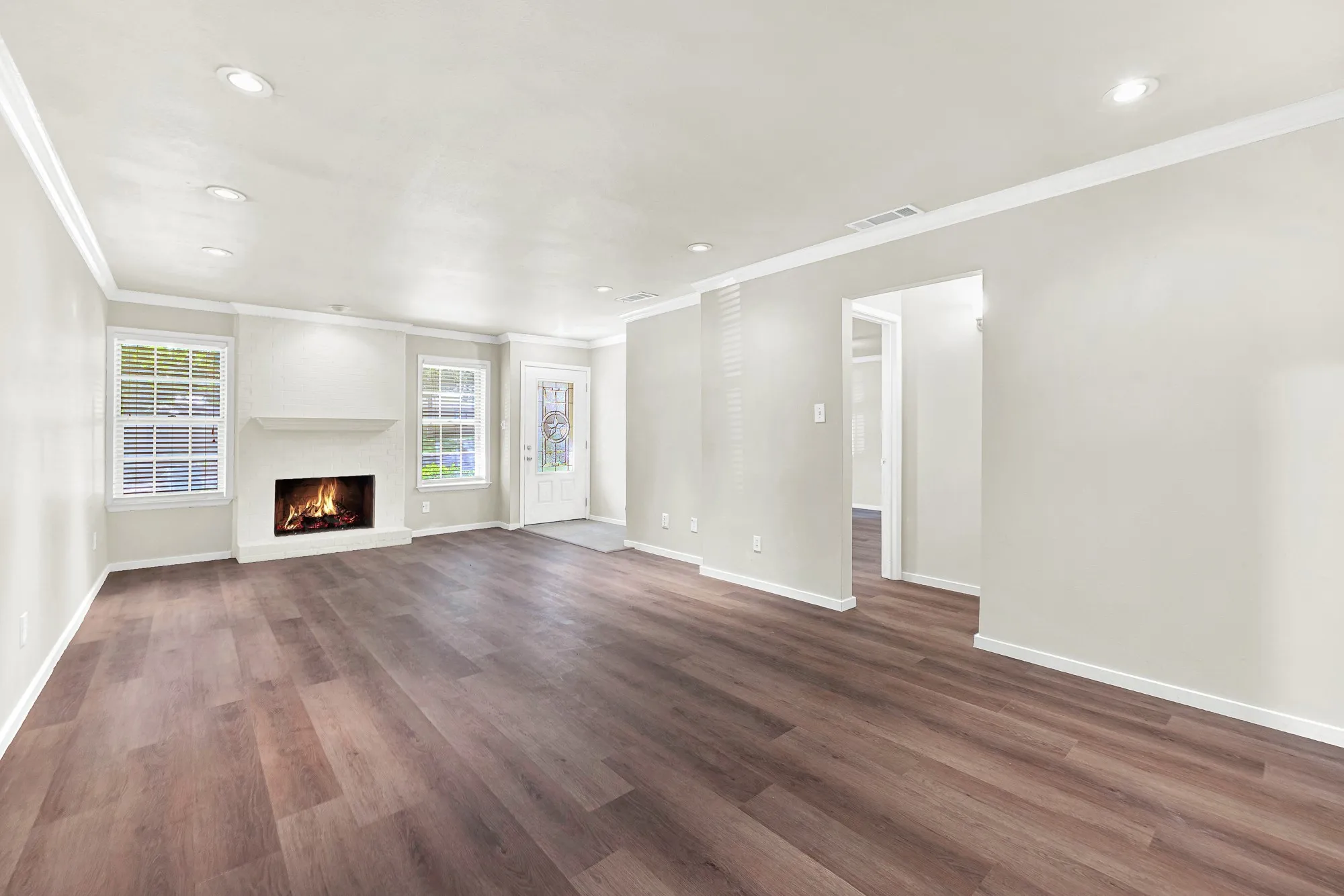 Spacious living area featuring wood-finish flooring, recessed lighting, a fireplace with a mantel, and multiple windows