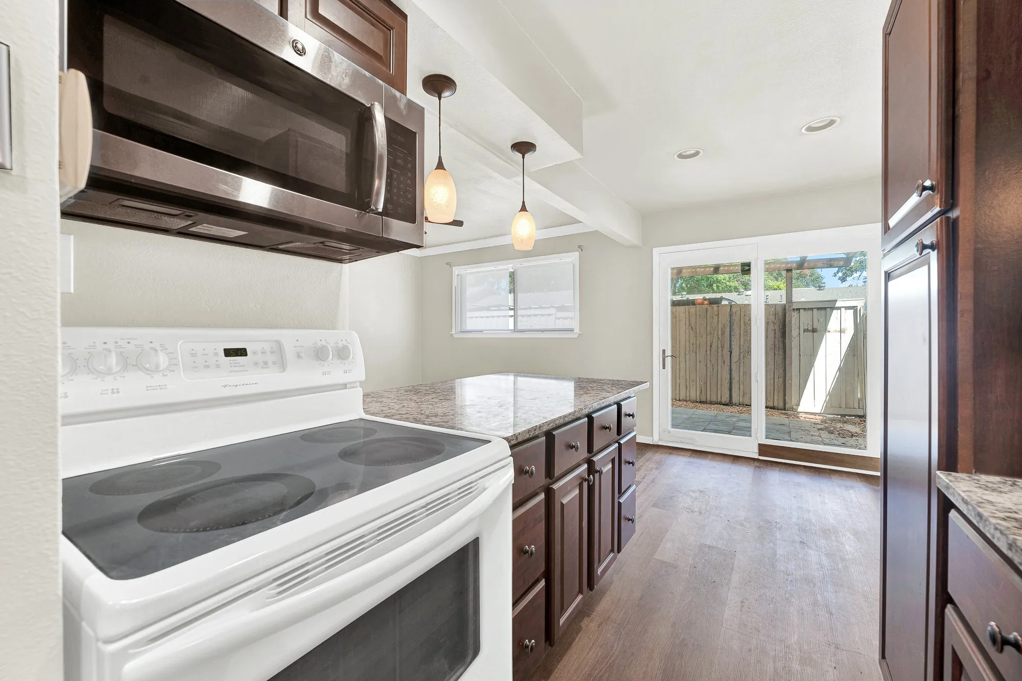 Kitchen featuring wood-finish flooring, dark wood cabinetry, granite-style countertops, stainless steel microwave, and glass sliding door