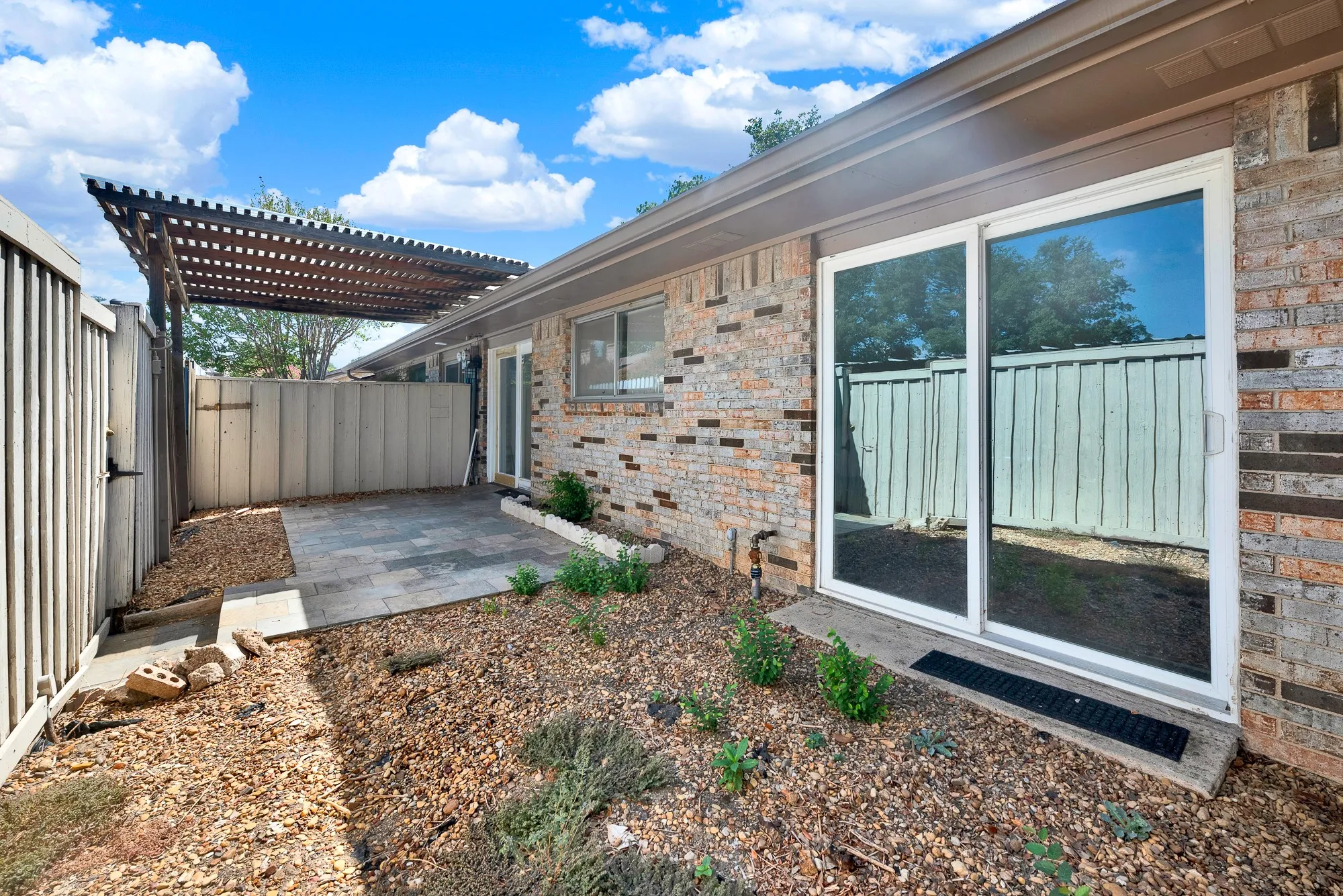 Brick exterior with sliding glass doors, a wood pergola, and a paved patio area