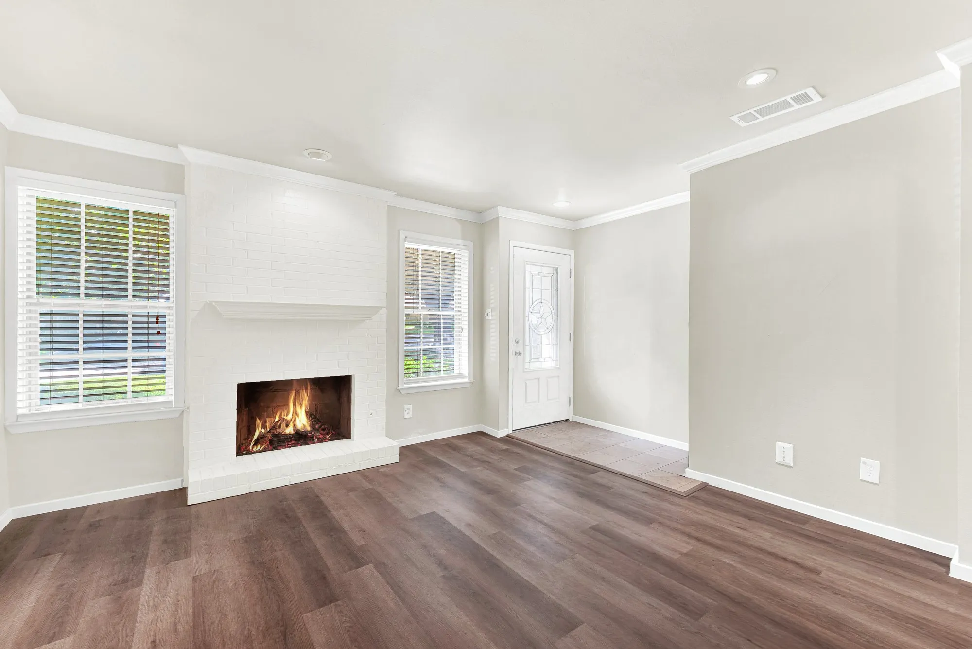 Spacious living area featuring wood-finish flooring, a white brick fireplace with mantel, and white crown molding