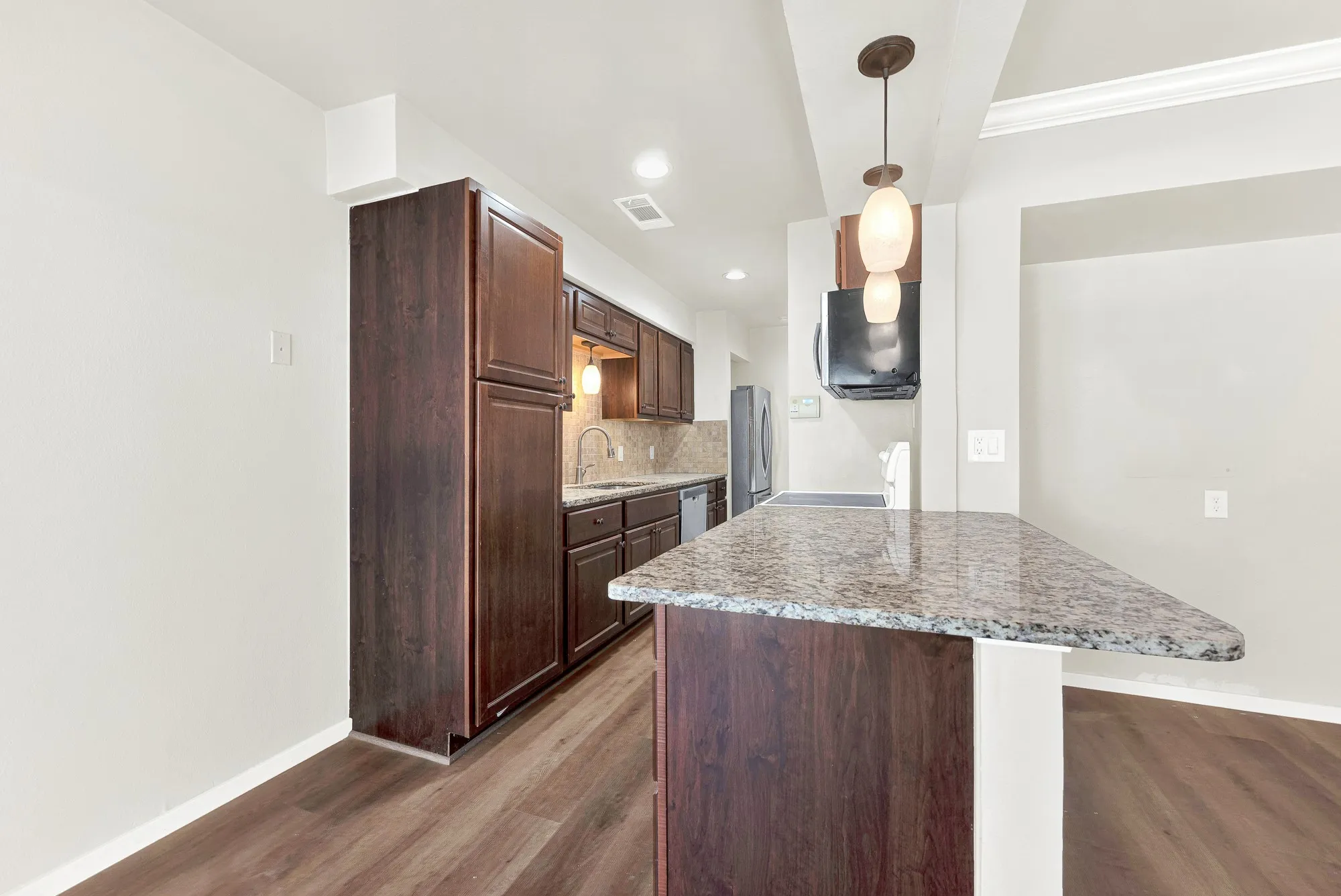 Kitchen with wood-finish flooring, dark wood cabinetry, a stone countertop island, recessed lighting, and a pendant light fixture