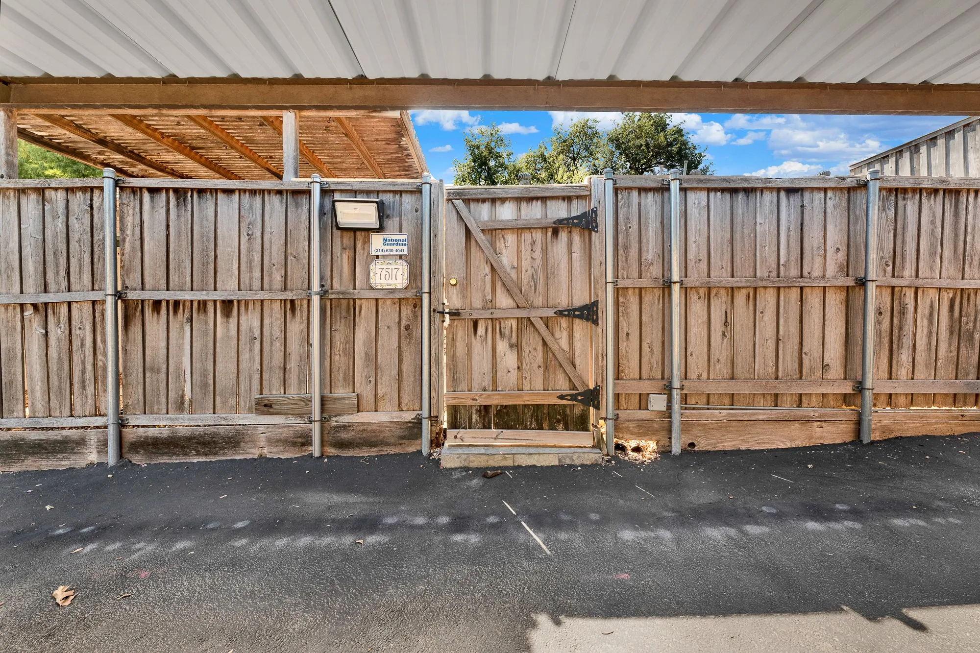 Wooden privacy fence with a secure gate, metal support posts, and an overhead carport structure