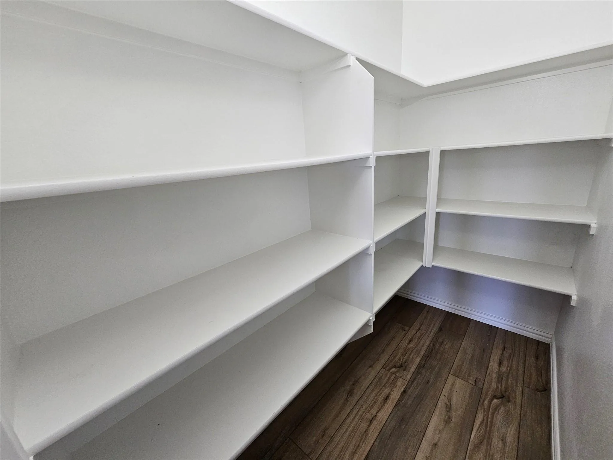 Built-in white shelving, multi-level storage, corner shelving unit, and wood-finish flooring