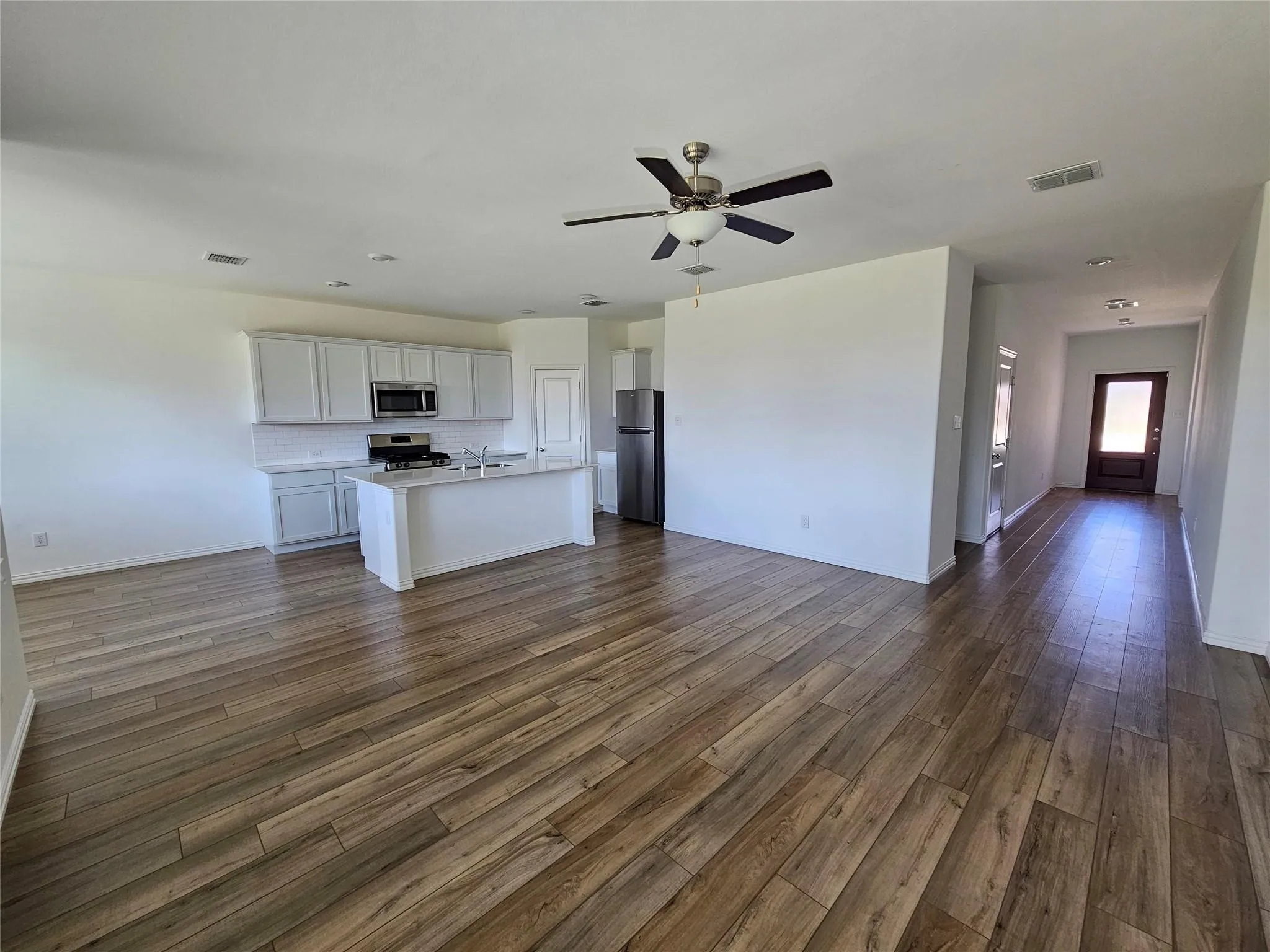 Wood-finish flooring throughout, kitchen with white cabinetry, stainless steel appliances, and a central island