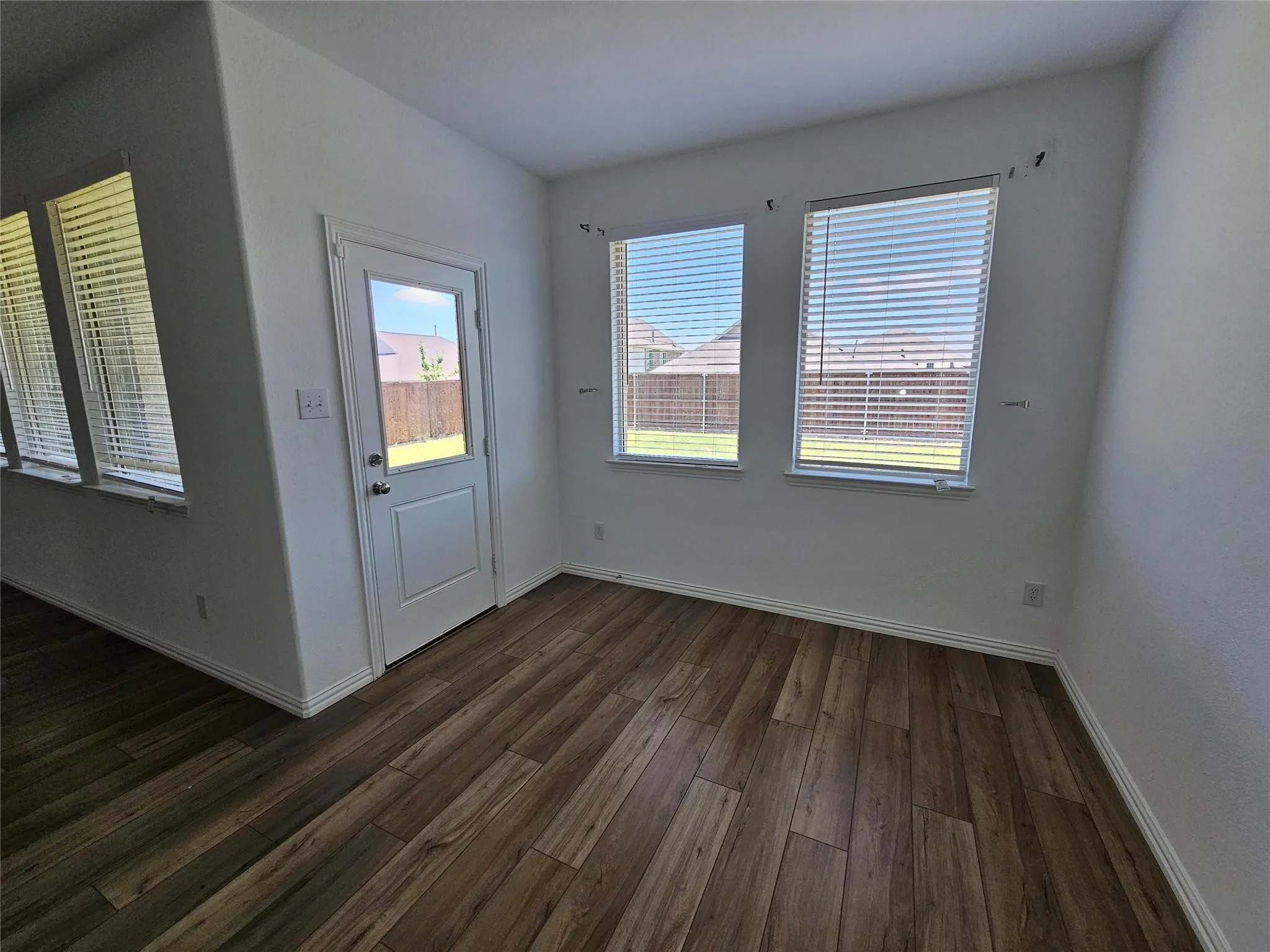 Wood-finish flooring, white trim, multiple windows with blinds, and an exterior door with glass paneling