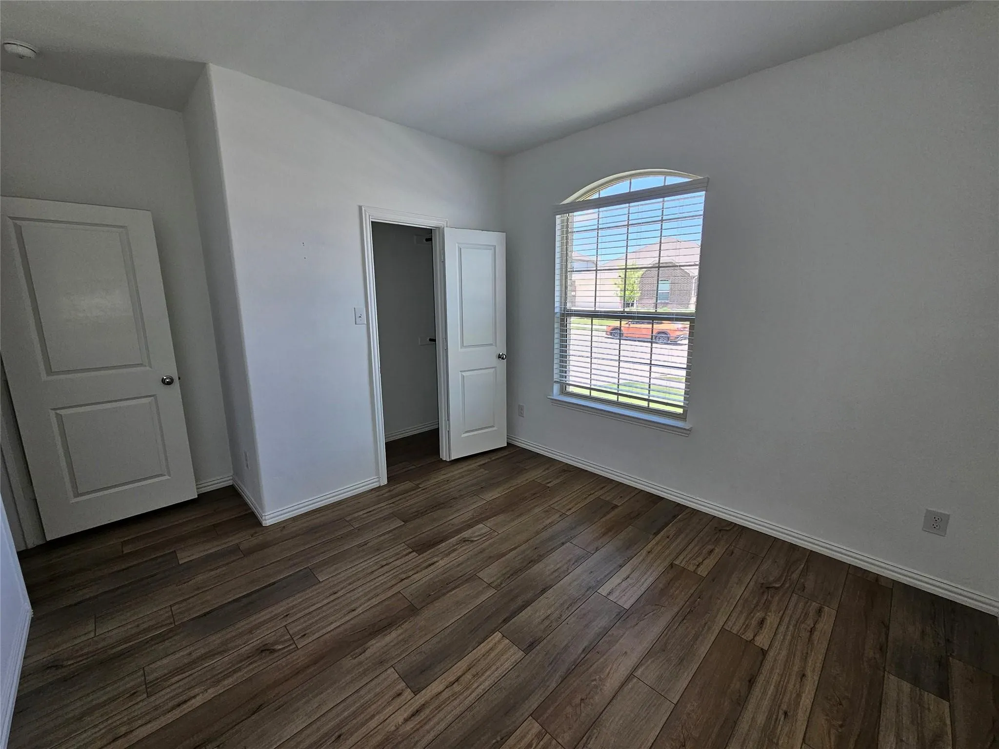 Wood-finish flooring, arched window, privacy blinds, and white paneled doors