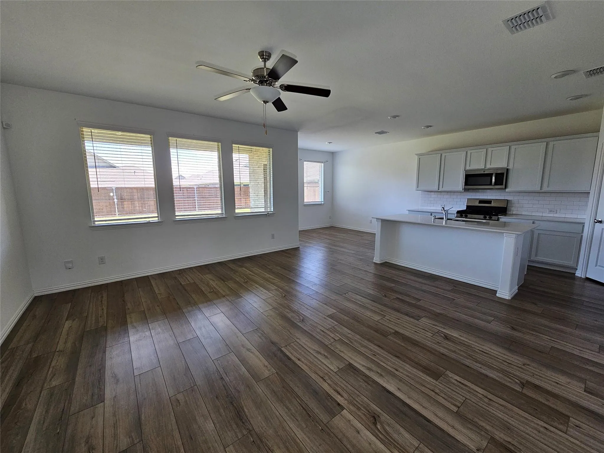 Open-concept living area with wood-finish flooring, a contemporary ceiling fan, and multiple windows