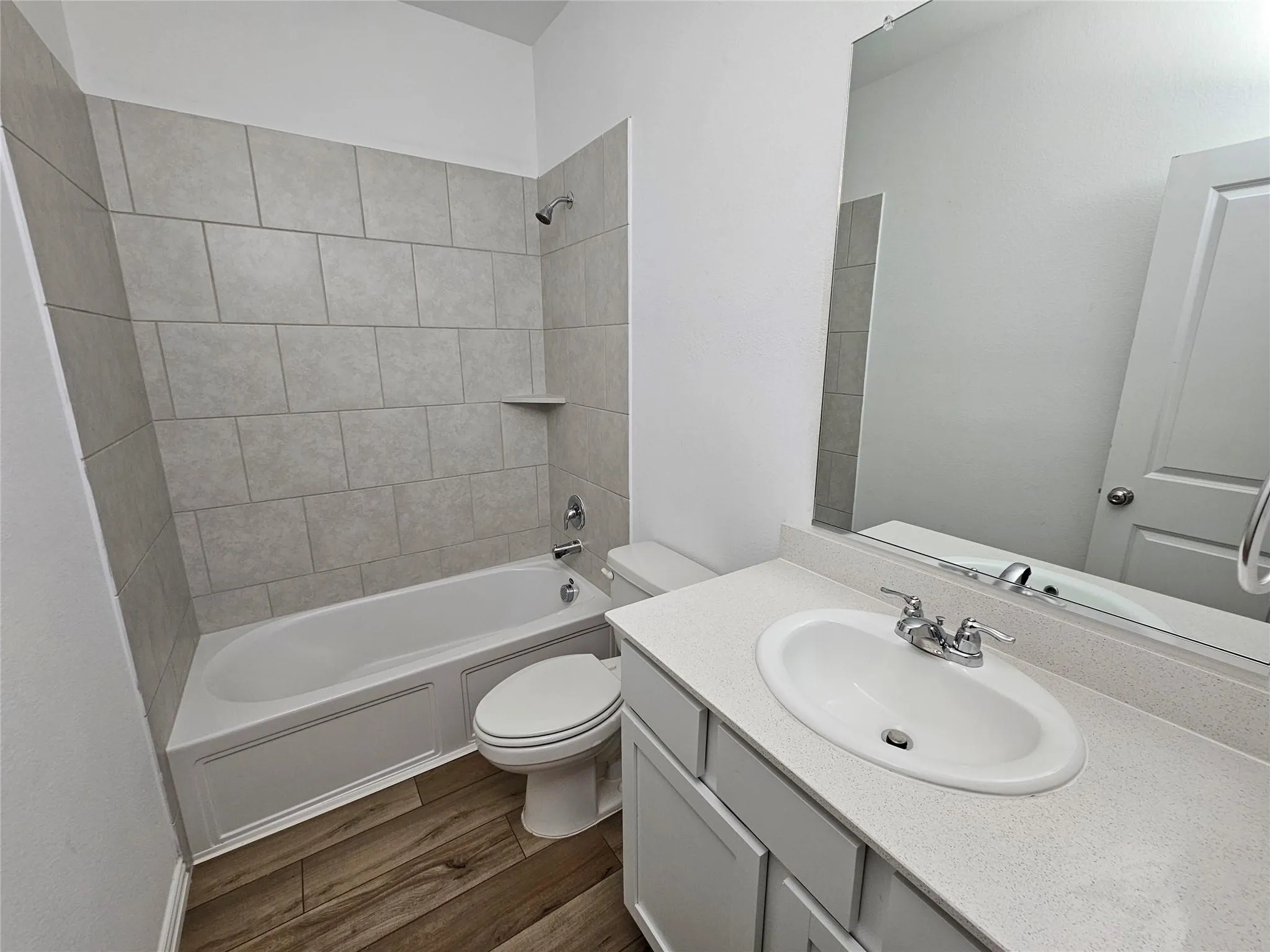 Full bathroom with a built-in tub/shower combination, tile surround, and wood-finish flooring