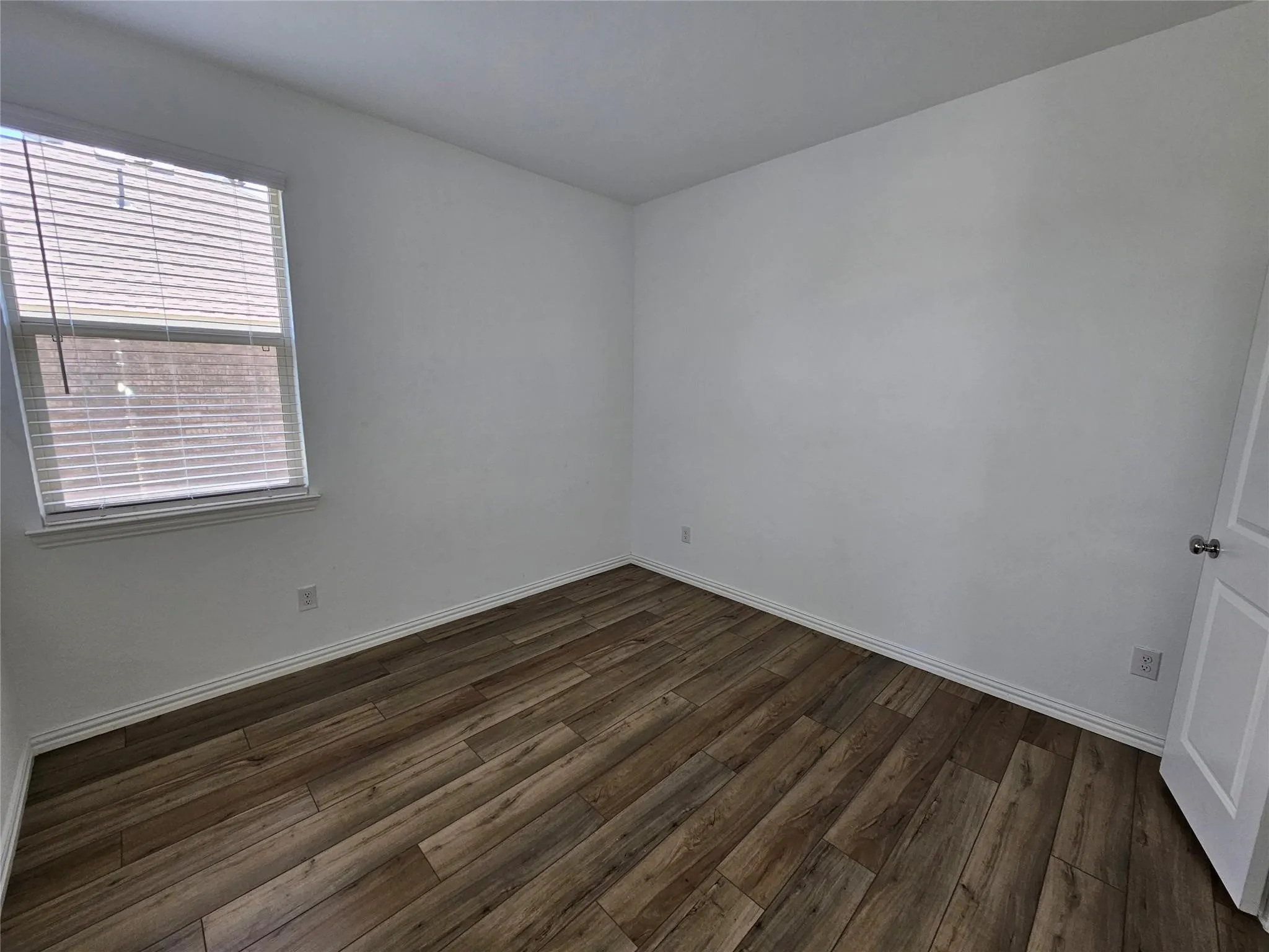 Wood-finish flooring with white walls and a single window featuring blinds