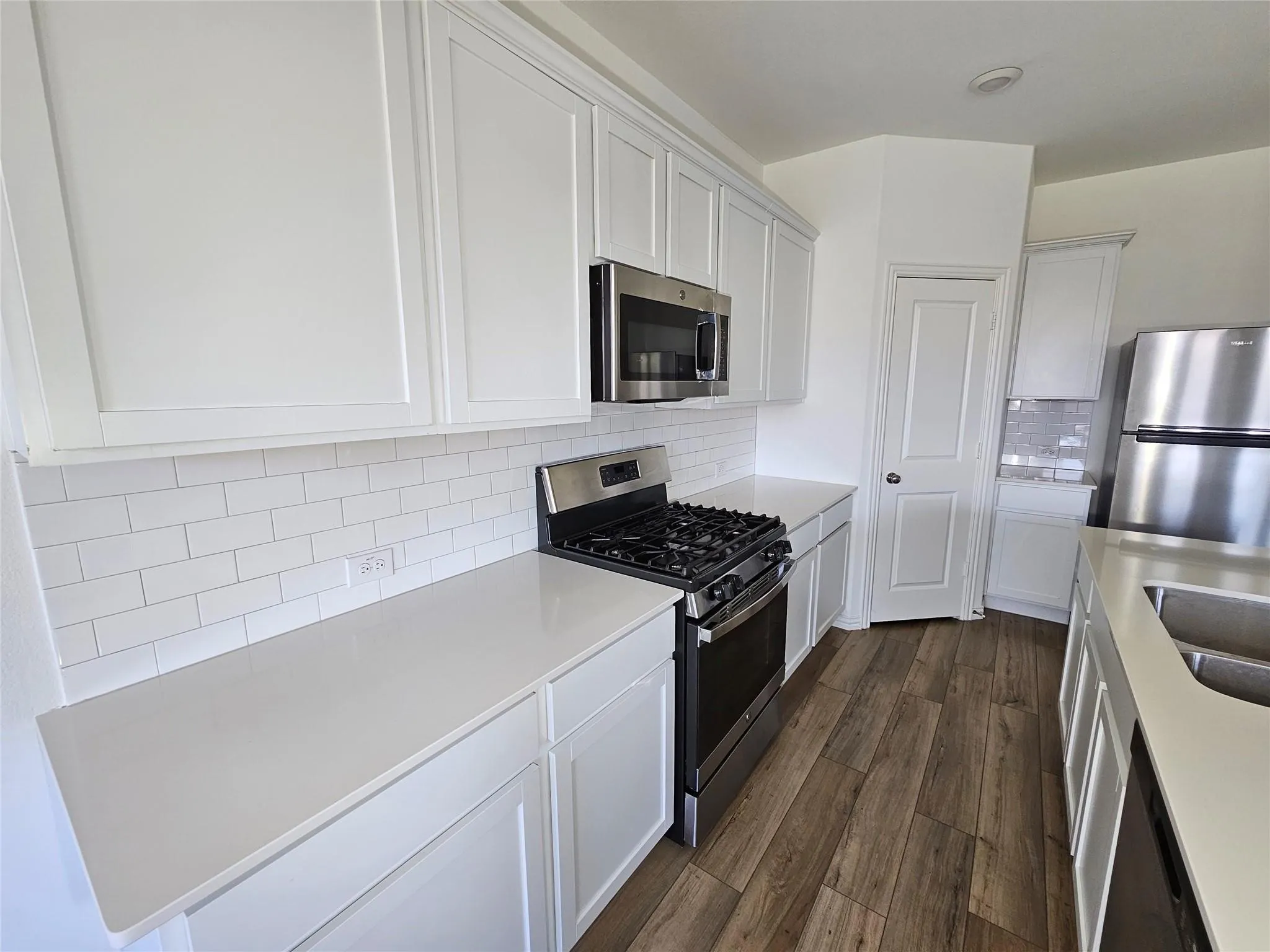 White shaker cabinetry, light-toned countertops, white subway tile backsplash, stainless steel appliances, and wood-finish flooring