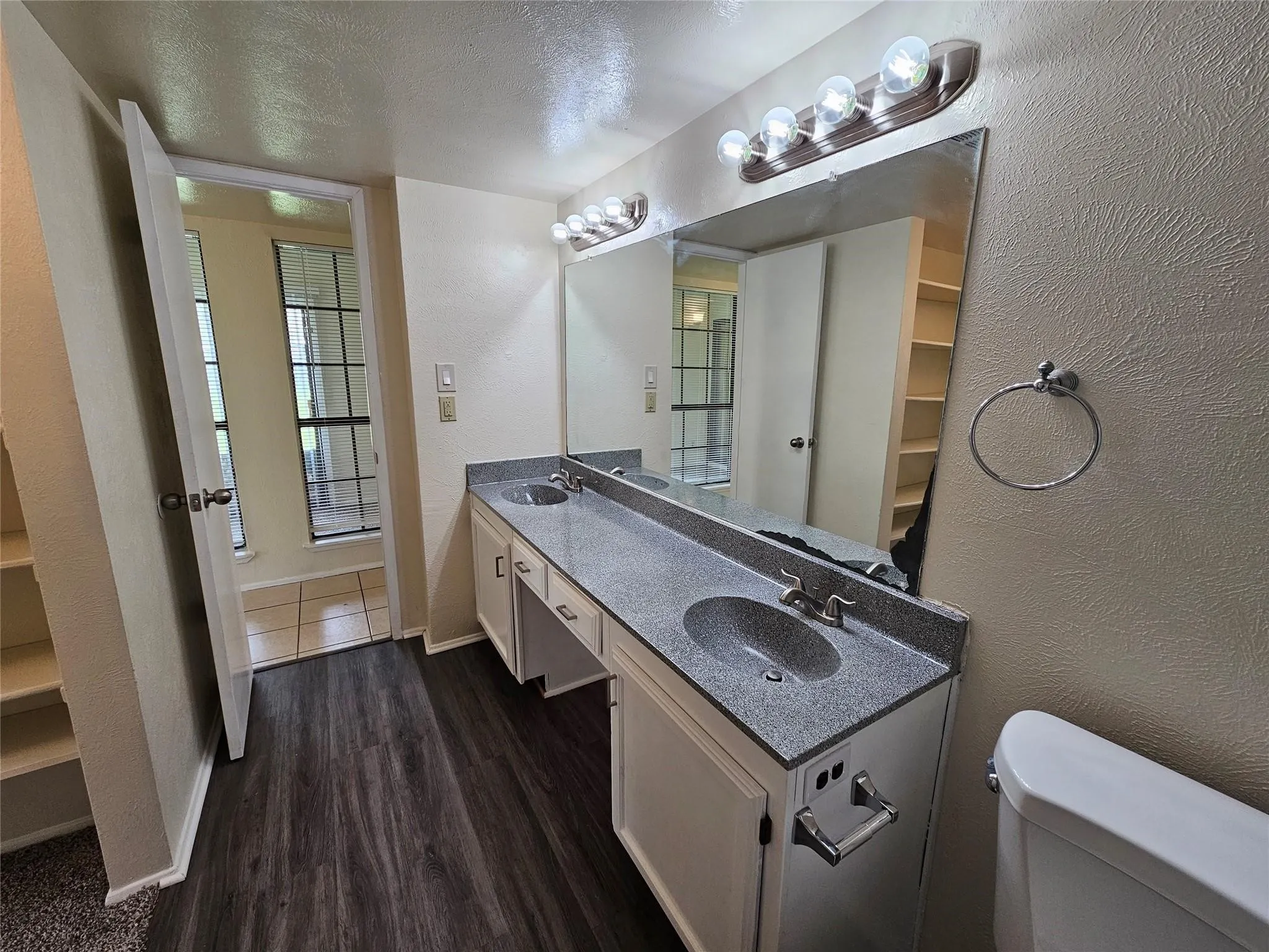 Dual sink vanity with dark-flecked countertop, wood-finish flooring, and built-in shelving