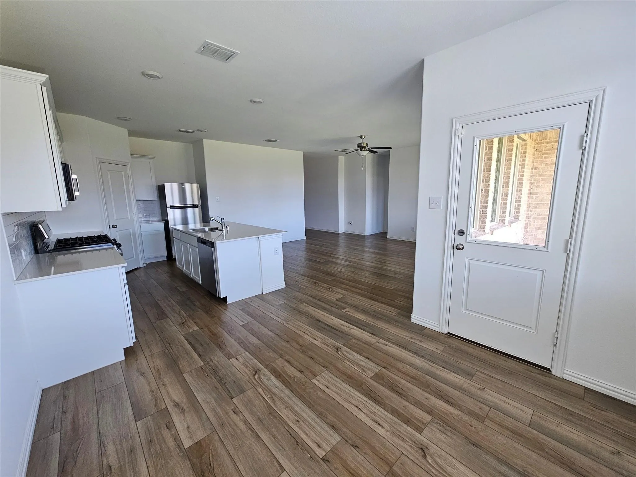 Kitchen featuring wood-finish flooring, white cabinetry, stainless steel appliances, and a central island with a sink