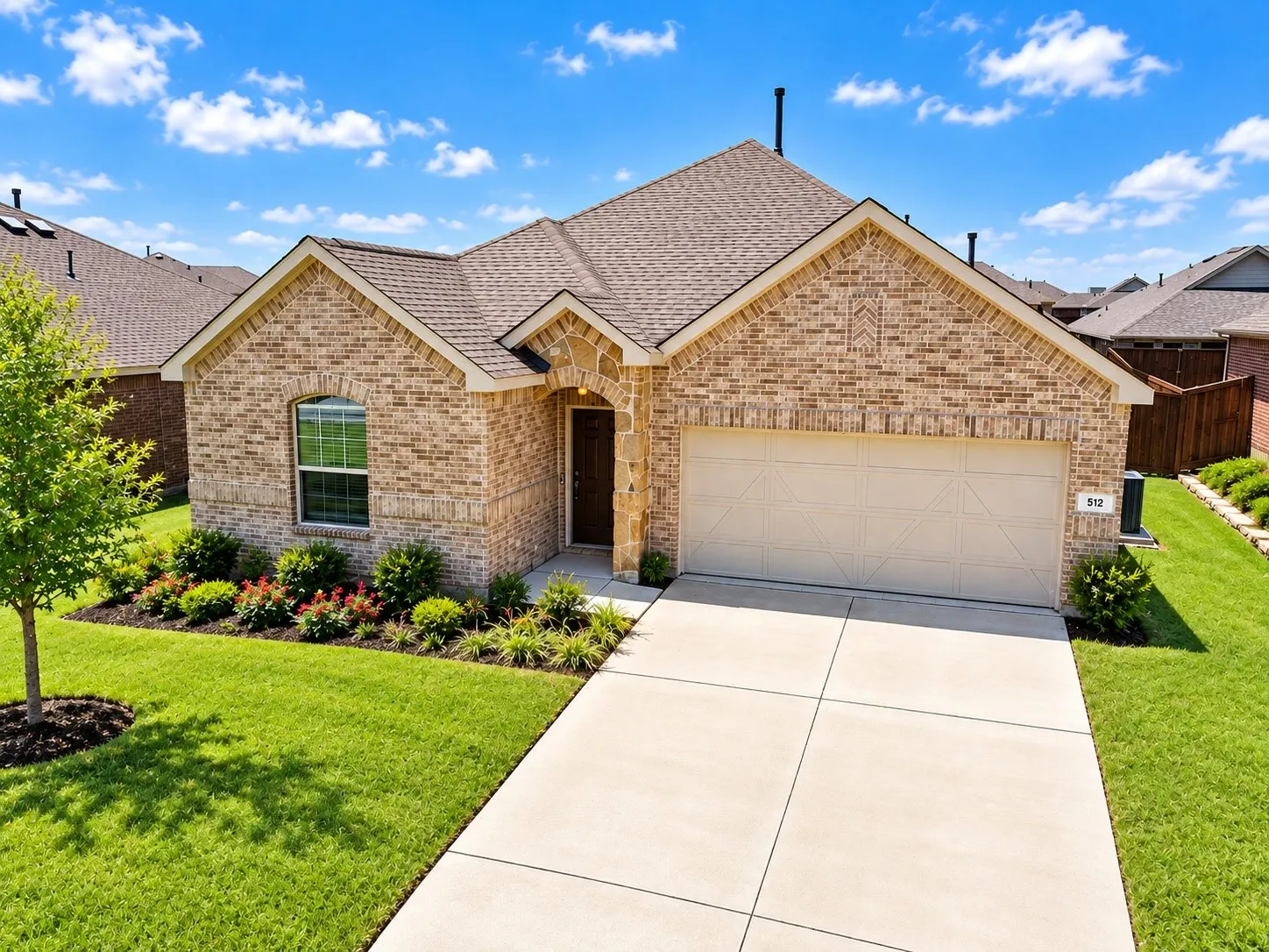 Brick exterior with stone accents, an arched entryway, an attached two-car garage, manicured landscaping, and a concrete driveway