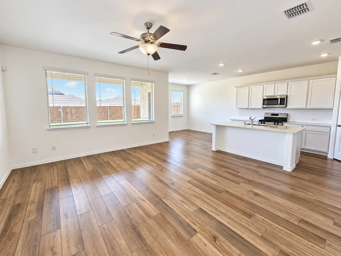 Open concept living area featuring wood-finish flooring, a ceiling fan with integrated lighting, and multiple windows with blinds