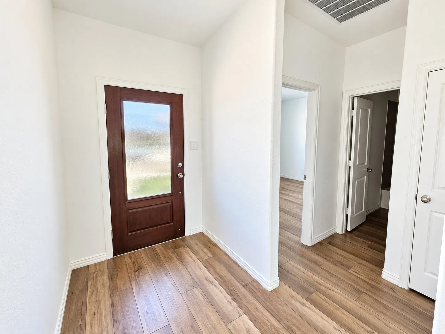 Wood-finish flooring, white wall paint, dark wood-paneled door with frosted glass, white trim