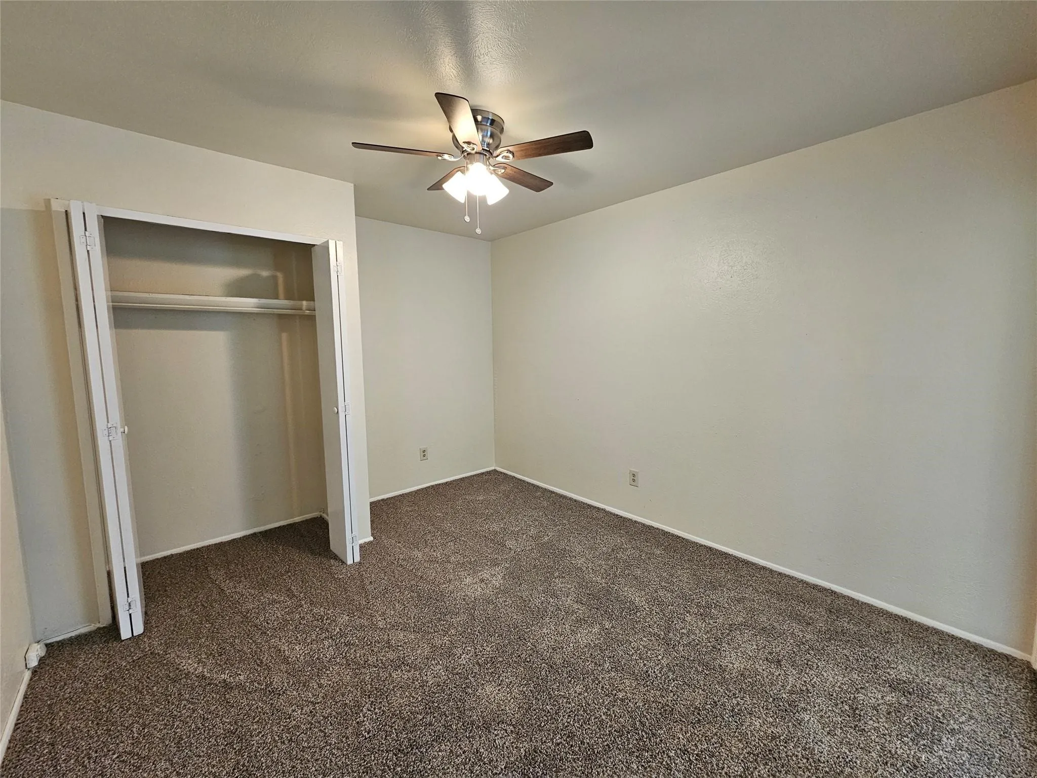 Textured carpeting, neutral wall finishes, ceiling-mounted fan with integrated lighting, and a bi-fold door closet