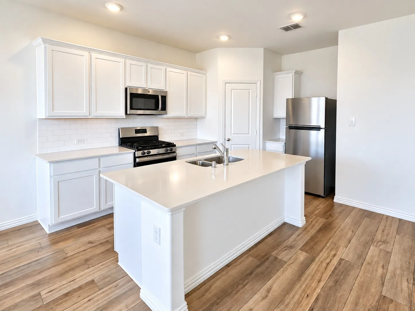 Kitchen featuring wood-finish flooring, white cabinetry, a central island with an integrated sink, stainless steel appliances, and subway tile backsplash