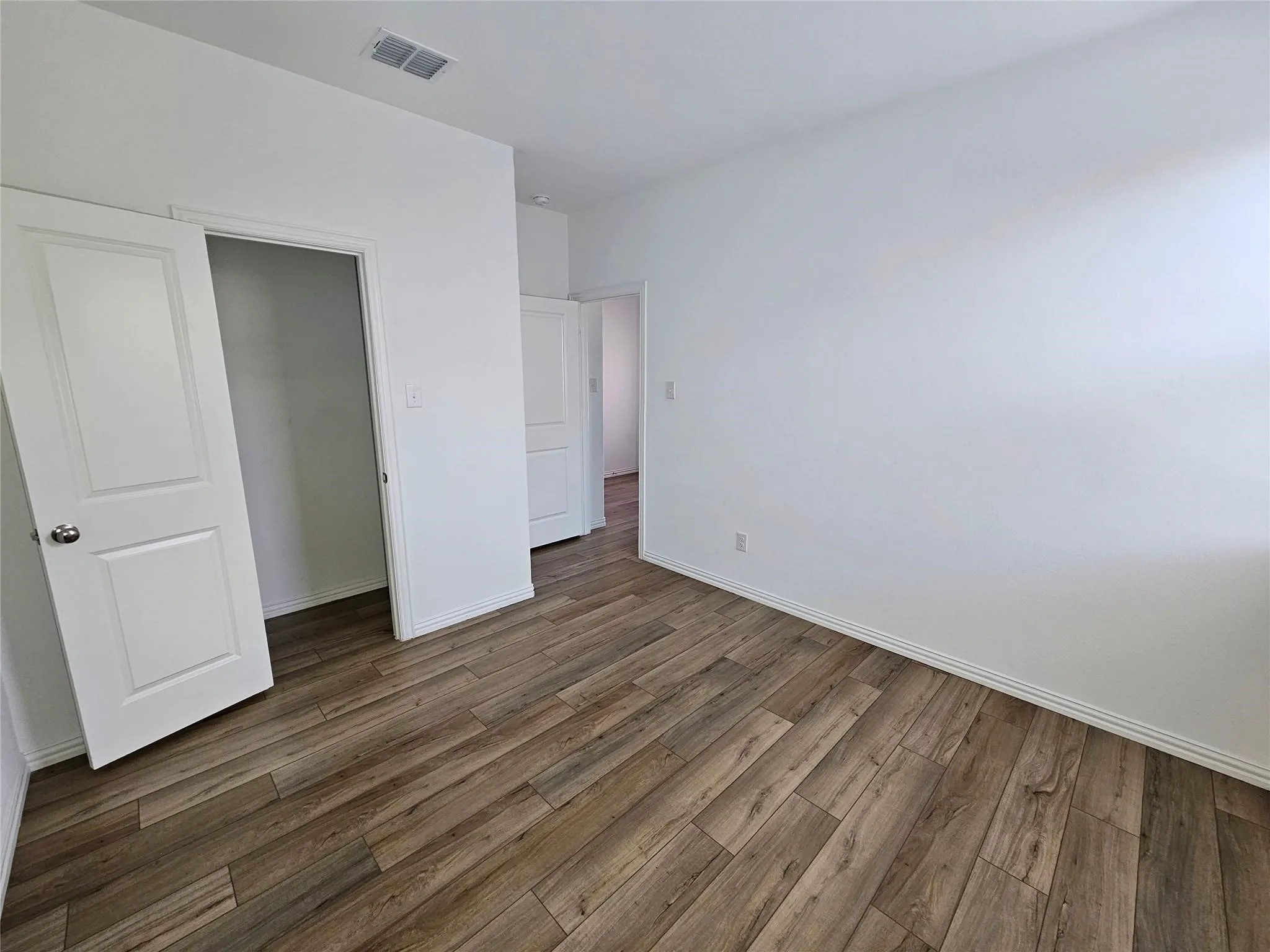 Wood-finish flooring, white painted walls, white interior doors, and a neutral ceiling