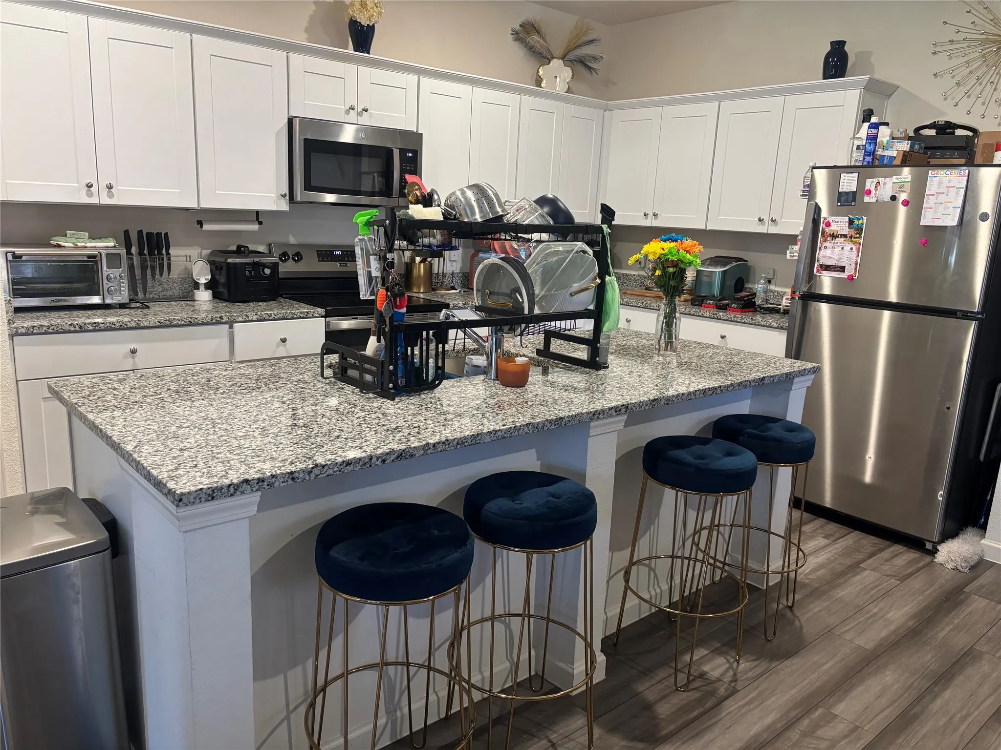 Kitchen featuring white cabinetry, light-toned countertops, stainless steel appliances, a center island with seating, and wood-finish flooring