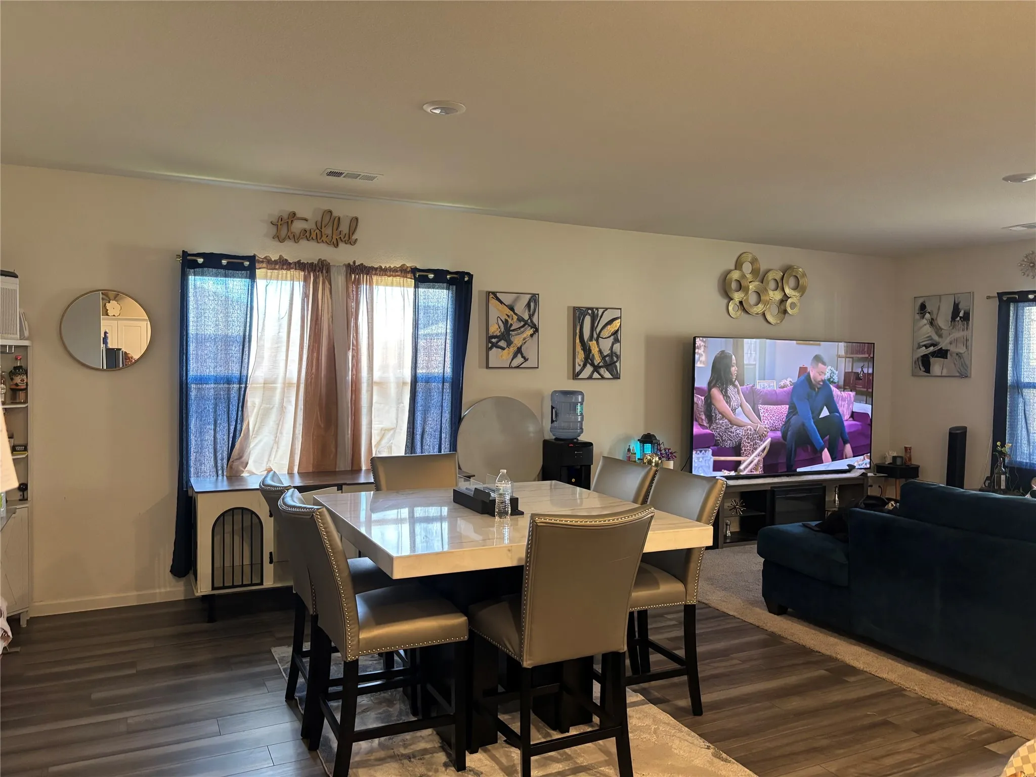 Wood-finish flooring, recessed ceiling lighting, light-toned walls, and multiple windows with curtain rods