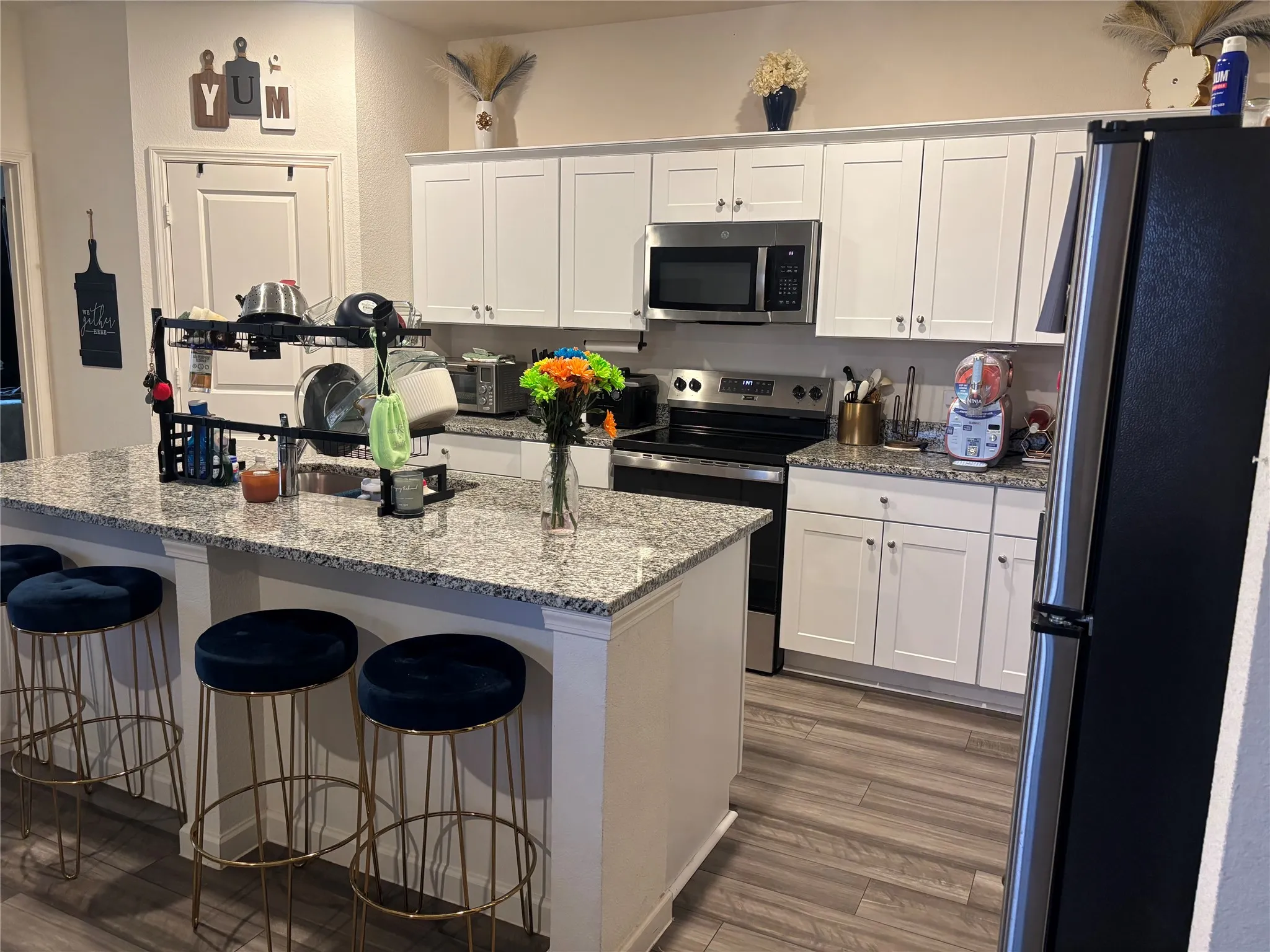 Spacious kitchen island with granite countertops, wood-finish flooring, white cabinetry, and stainless steel appliances