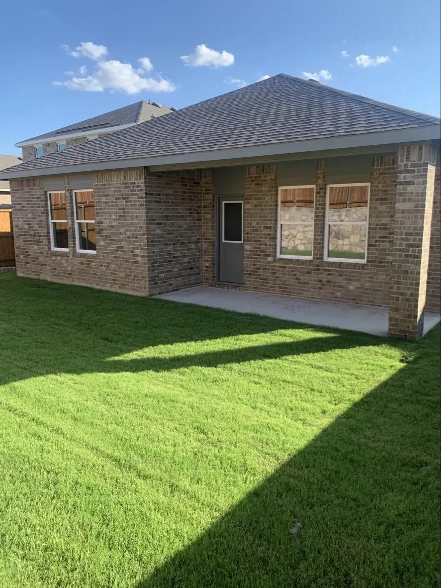 Brick exterior with a covered patio, a dark shingle roof, and a grassy backyard