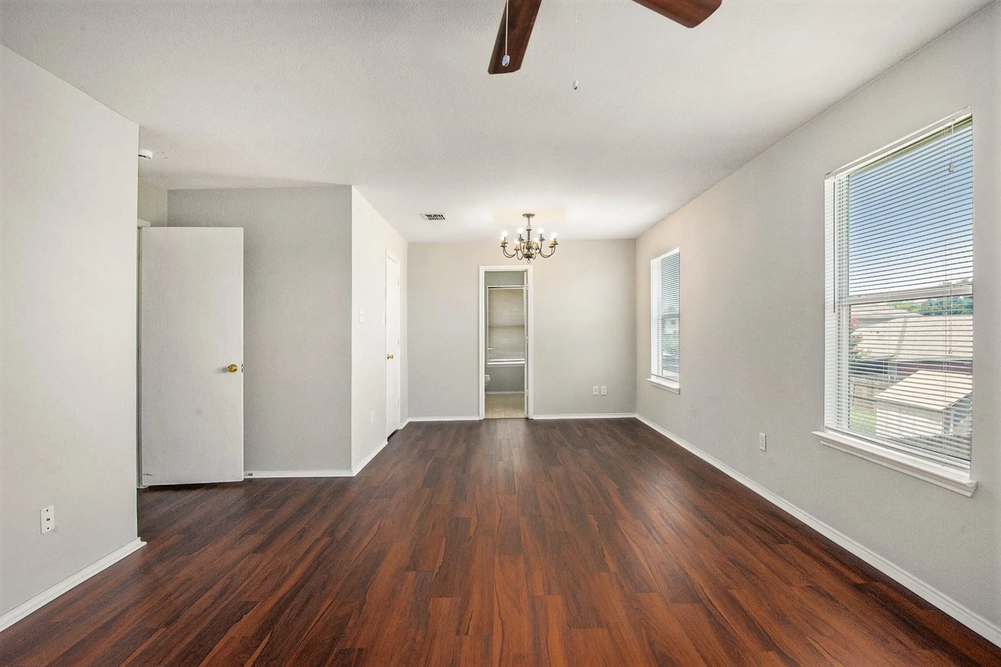 Empty room featuring dark wood-style floors, ceiling fan, and a chandelier