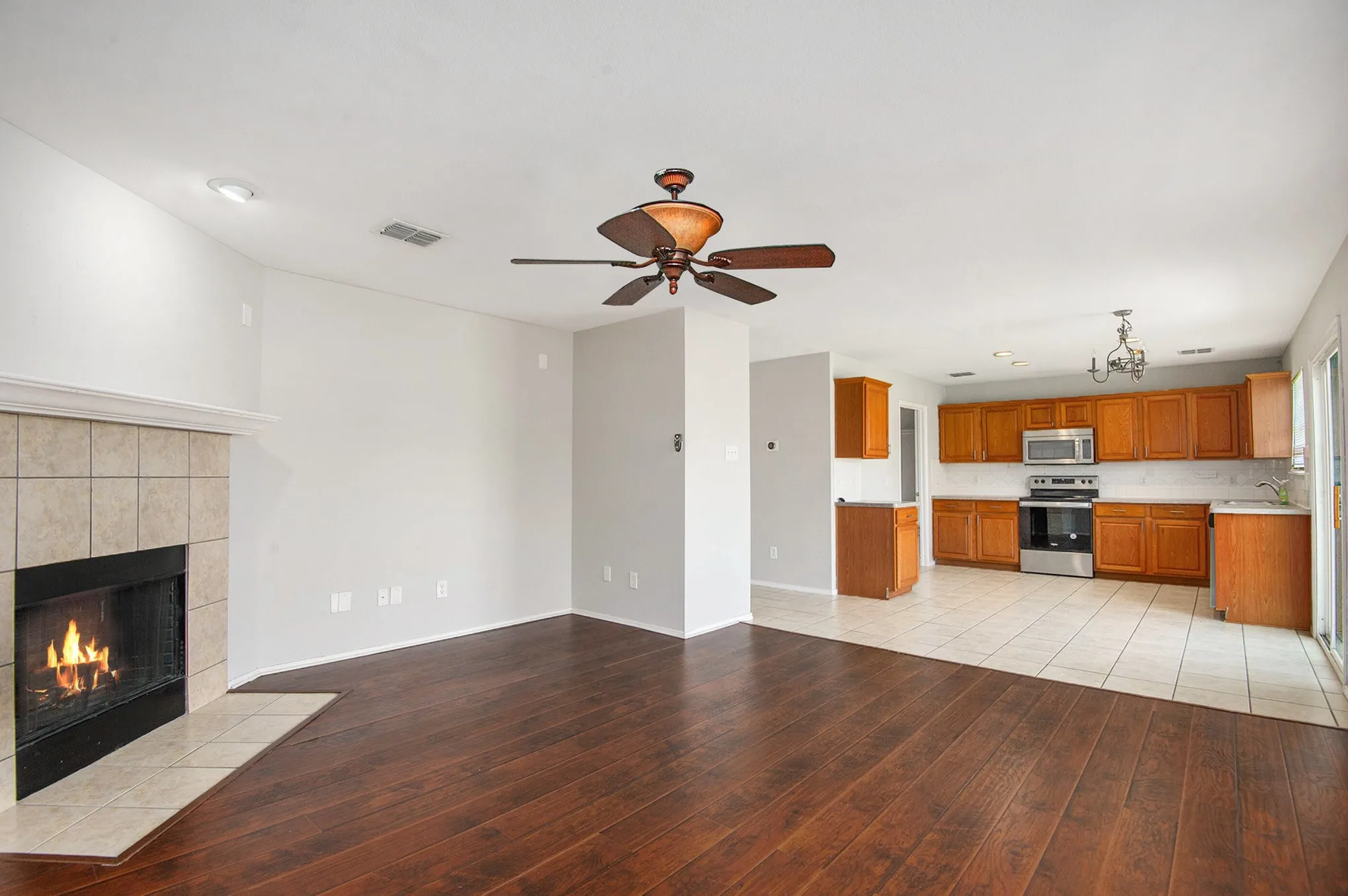Unfurnished living room with light wood finished floors, a tiled fireplace, and a ceiling fan