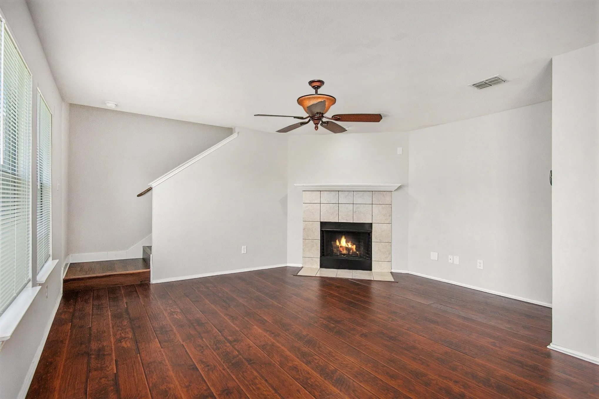 Unfurnished living room featuring hardwood / wood-style flooring, a ceiling fan, a tile fireplace, and stairway