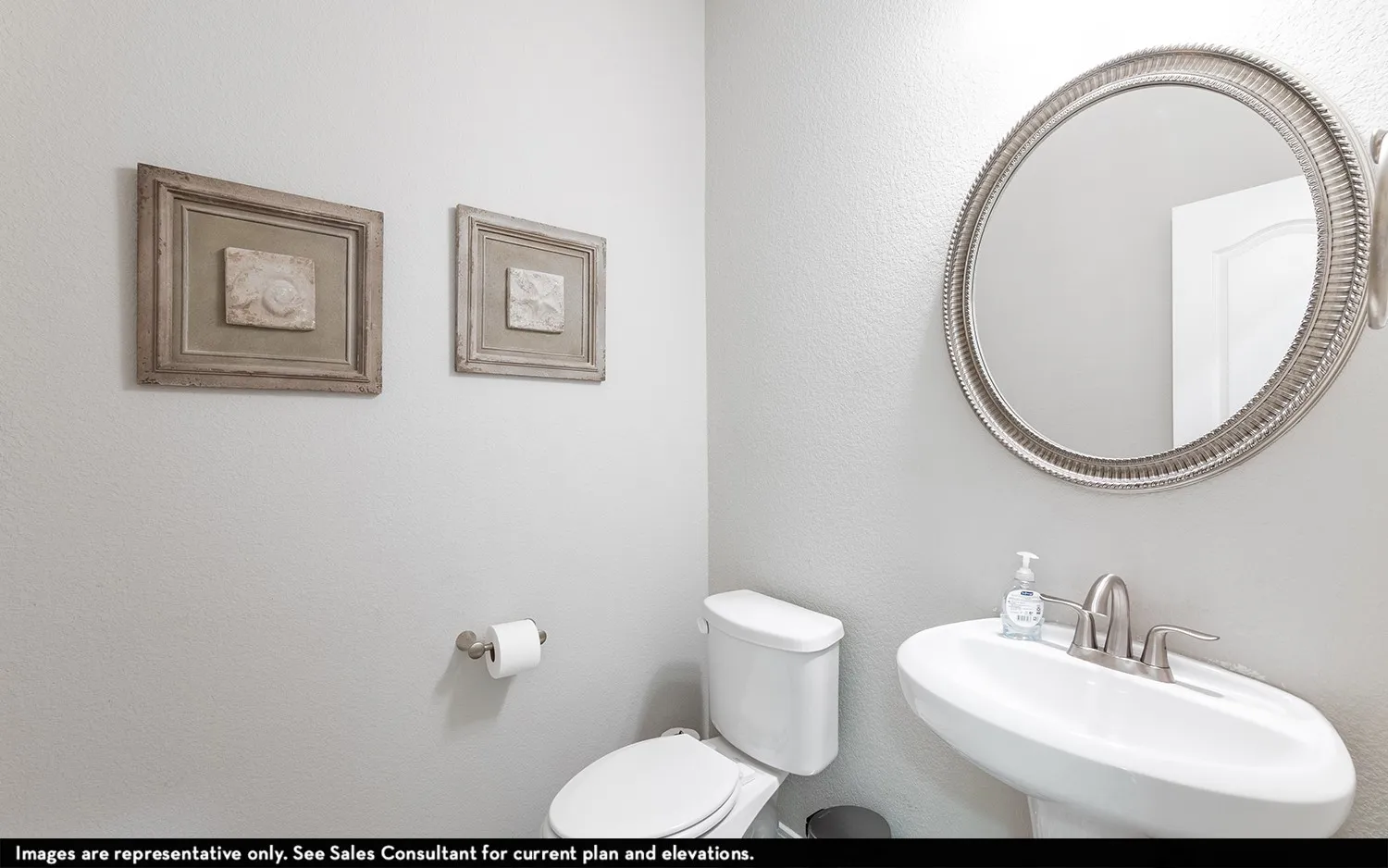 Pedestal sink with brushed nickel faucet, round framed mirror, and white toilet