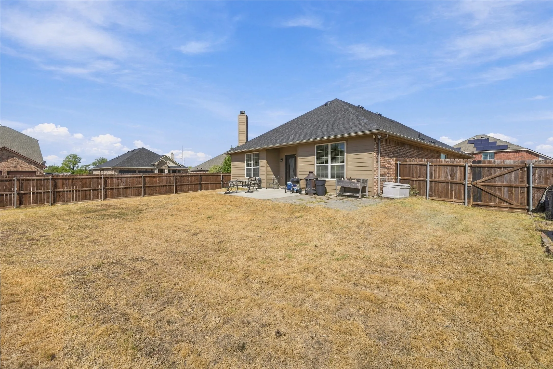 Expansive backyard featuring a privacy fence, concrete patio, and exterior lighting