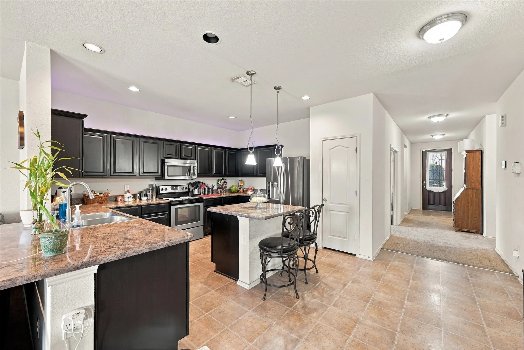 Kitchen featuring dark wood cabinetry, stainless steel appliances, a center island with pendant lighting, and tiled flooring