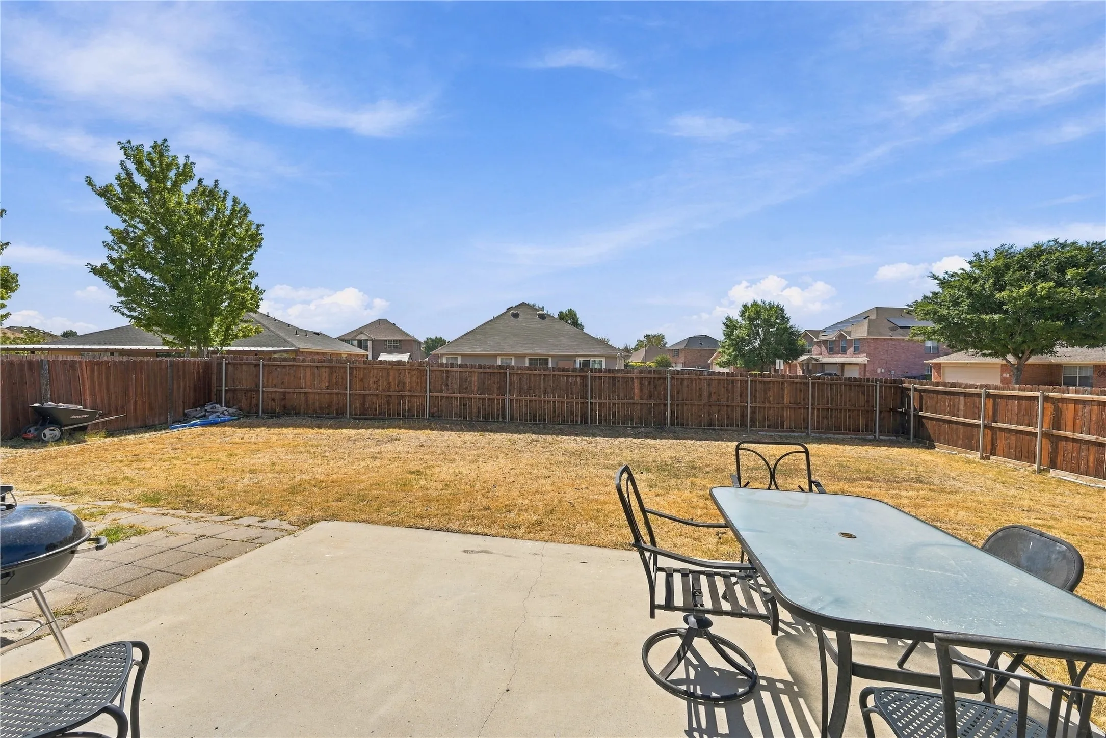 Expansive backyard with a concrete patio, wood privacy fencing, and mature trees