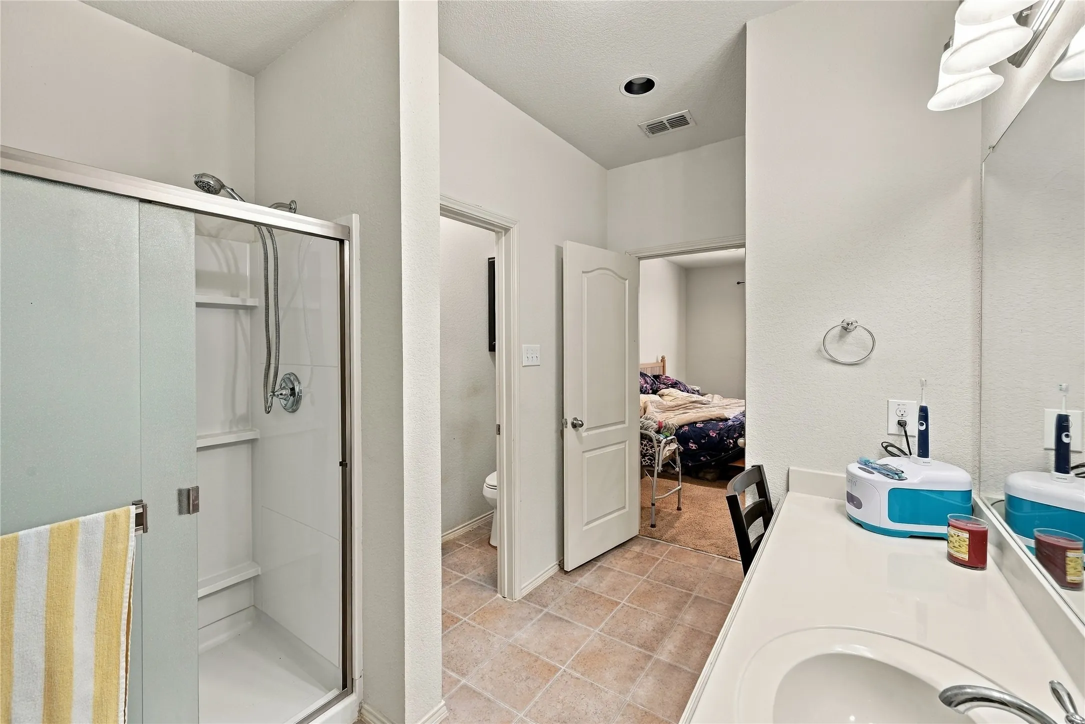 Walk-in shower with sliding glass door, single vanity with integrated sink, polished chrome fixtures, and tiled flooring